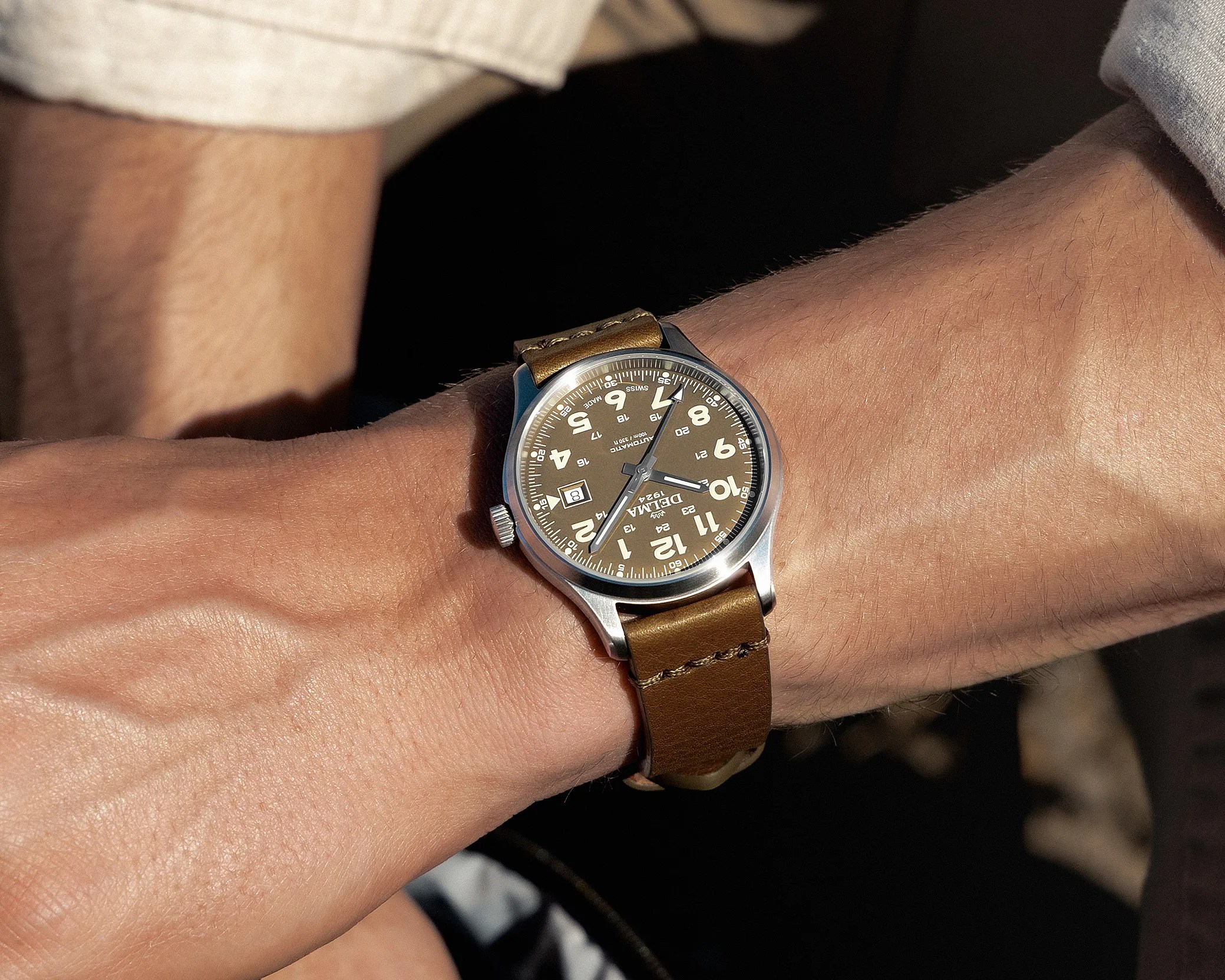 Silver watch with brown leather strap and beige dial showing date on a wrist.