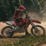 Person in red and black Ducati motocross gear riding a red dirt bike on a dirt trail.
