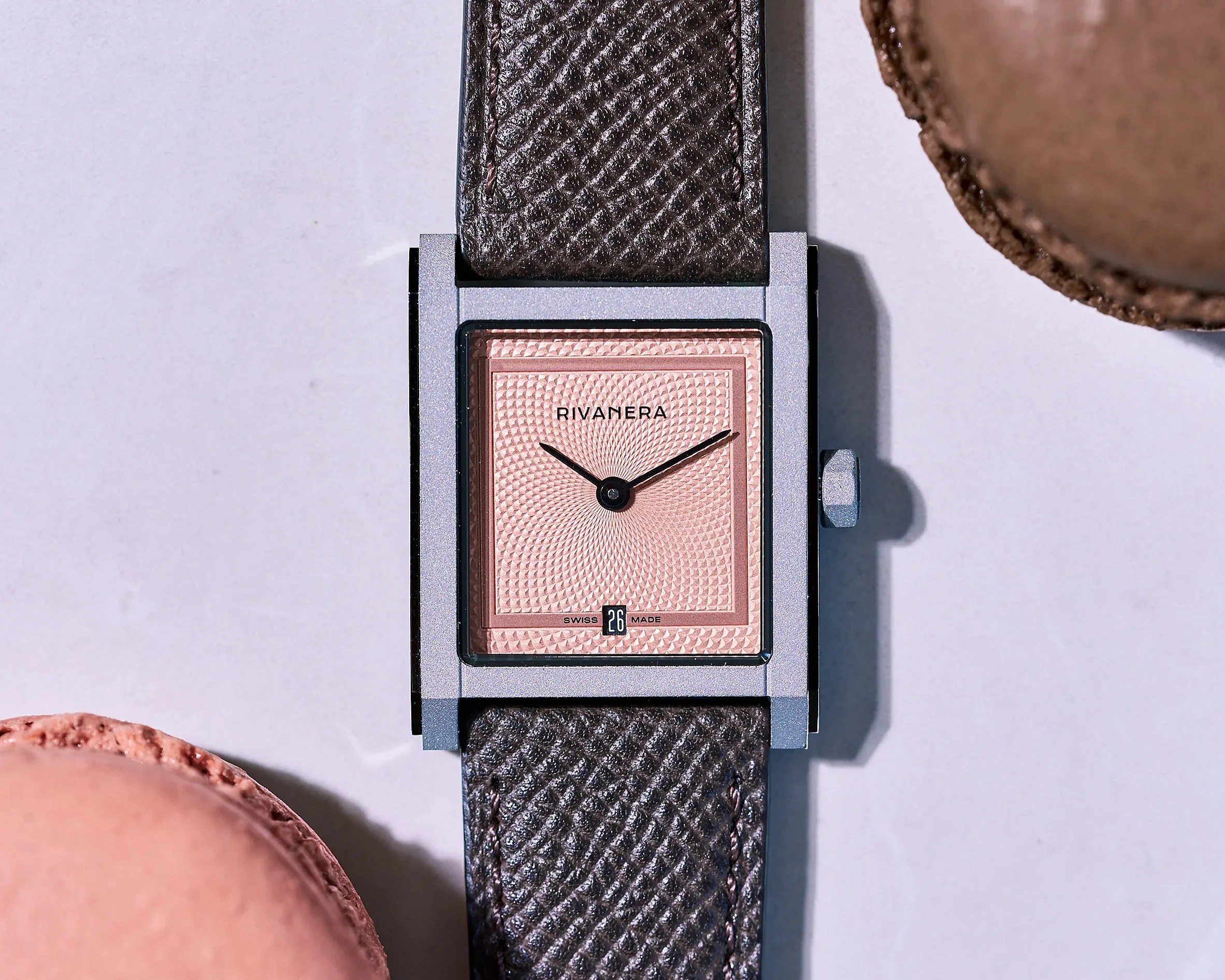 Rectangular wristwatch with a textured pink dial, black hands, date display, and dark brown leather strap.