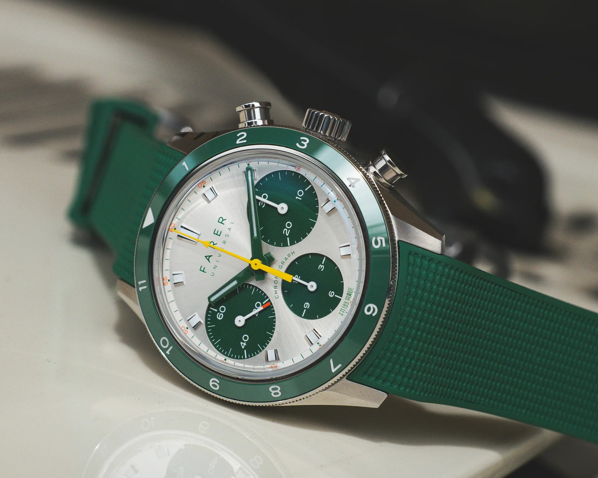 Silver chronograph watch with green bezel and subdials, yellow second hand, and green textured strap.