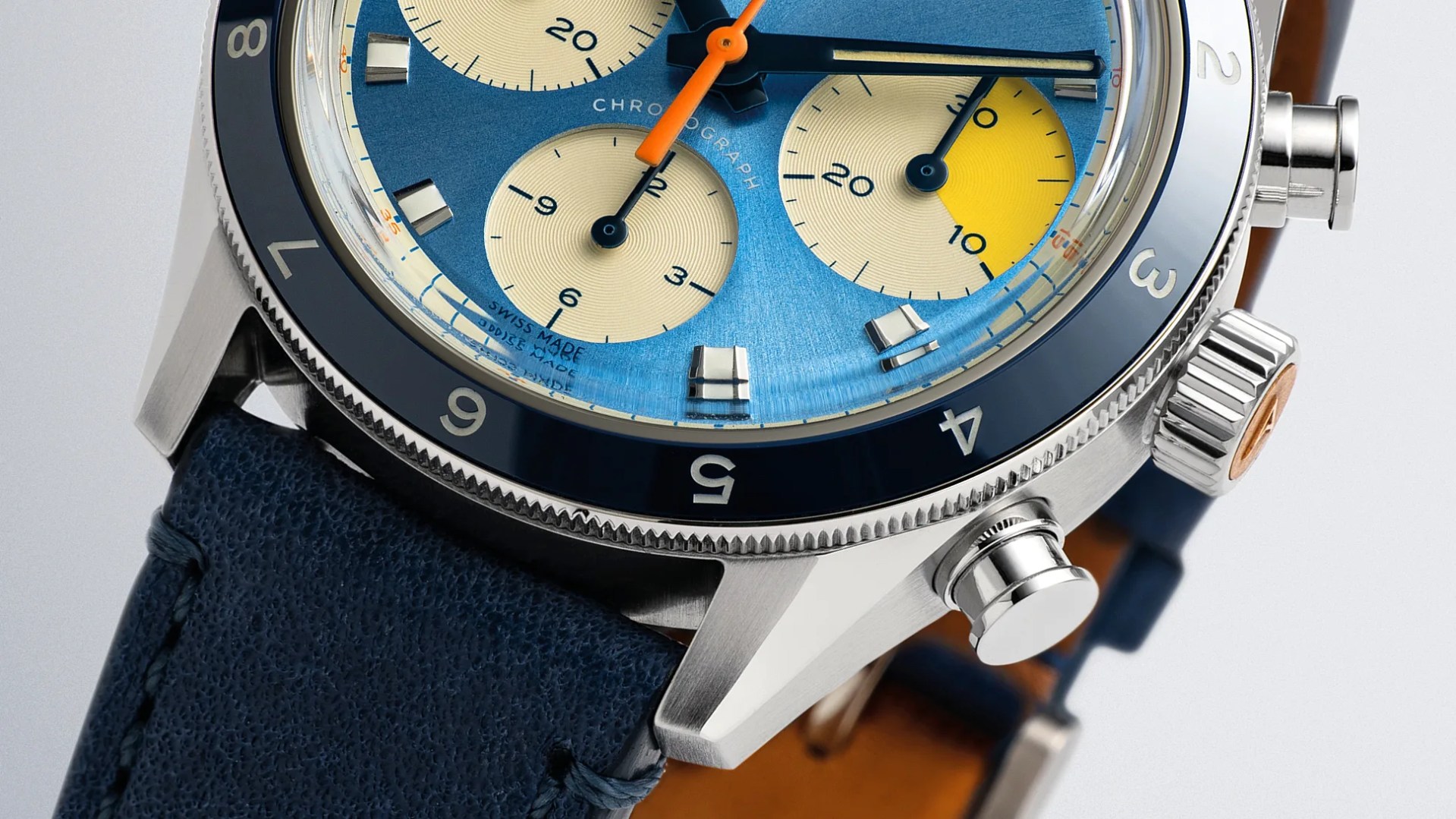 Close-up of a stainless steel chronograph watch with a blue dial, yellow subdial, and navy leather strap.