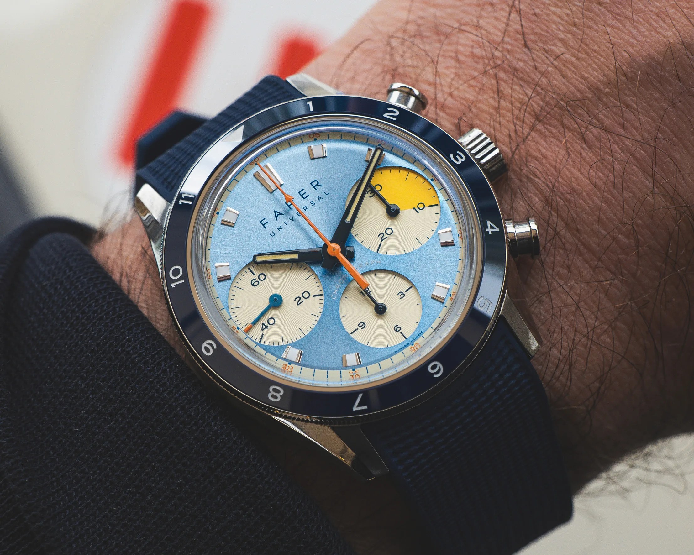 Blue-faced chronograph wristwatch with yellow subdials and black bezel on a wrist.