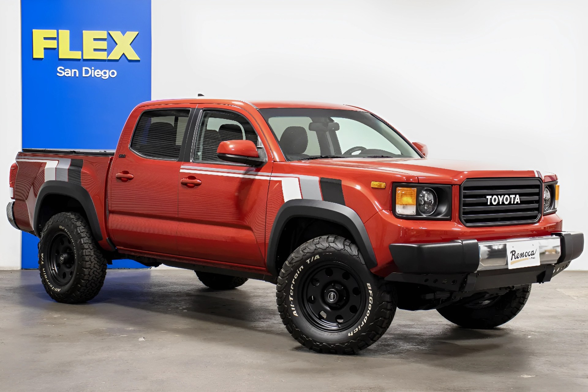 Red Toyota pickup truck with black grille and off-road tires parked indoors near a blue FLEX San Diego sign.