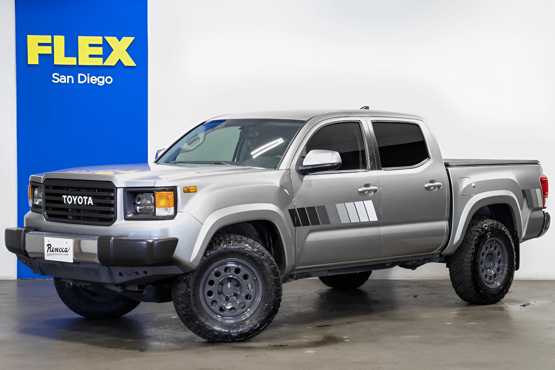 Silver Toyota pickup truck with black grille and off-road tires parked indoors near a blue and yellow FLEX San Diego sign.