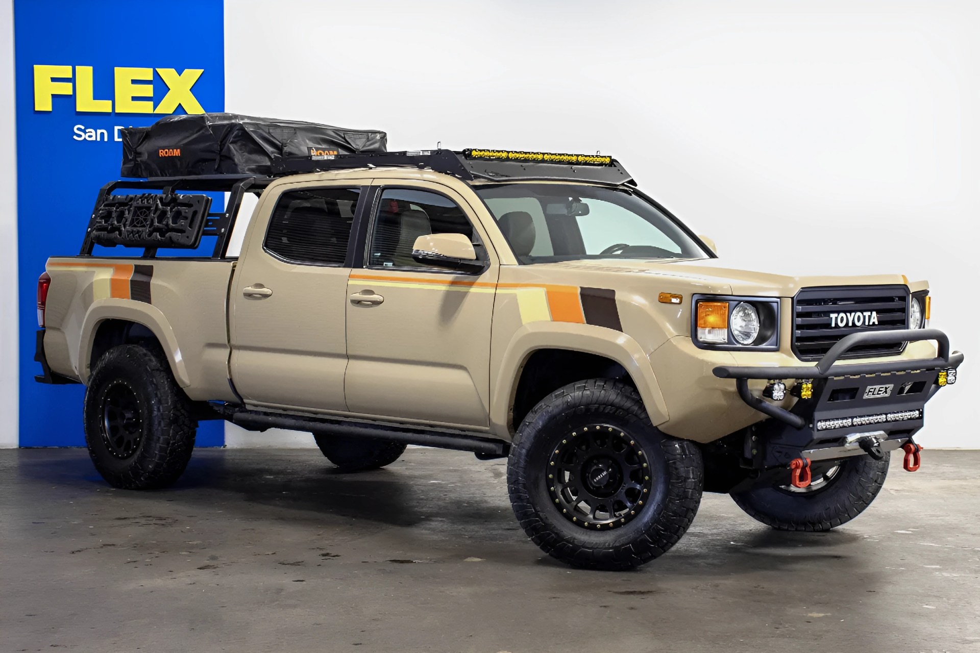 Beige Toyota pickup truck with off-road tires, roof rack, and camping gear mounted on the bed.