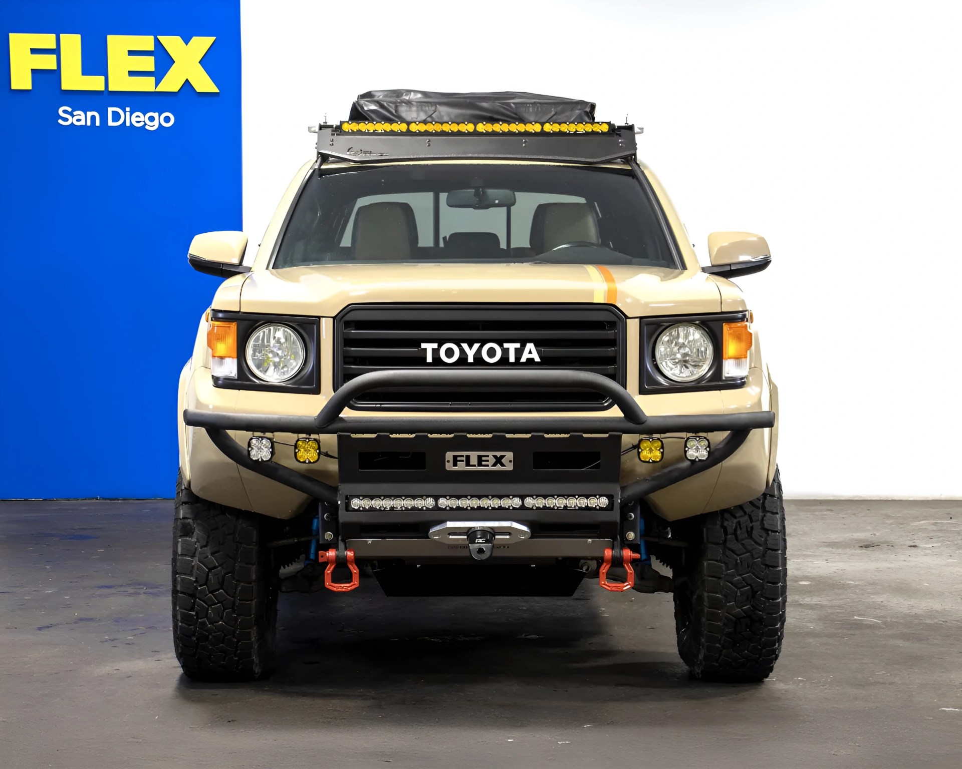Beige Toyota off-road vehicle with roof rack, yellow lights, and black bull bar in a studio setting.