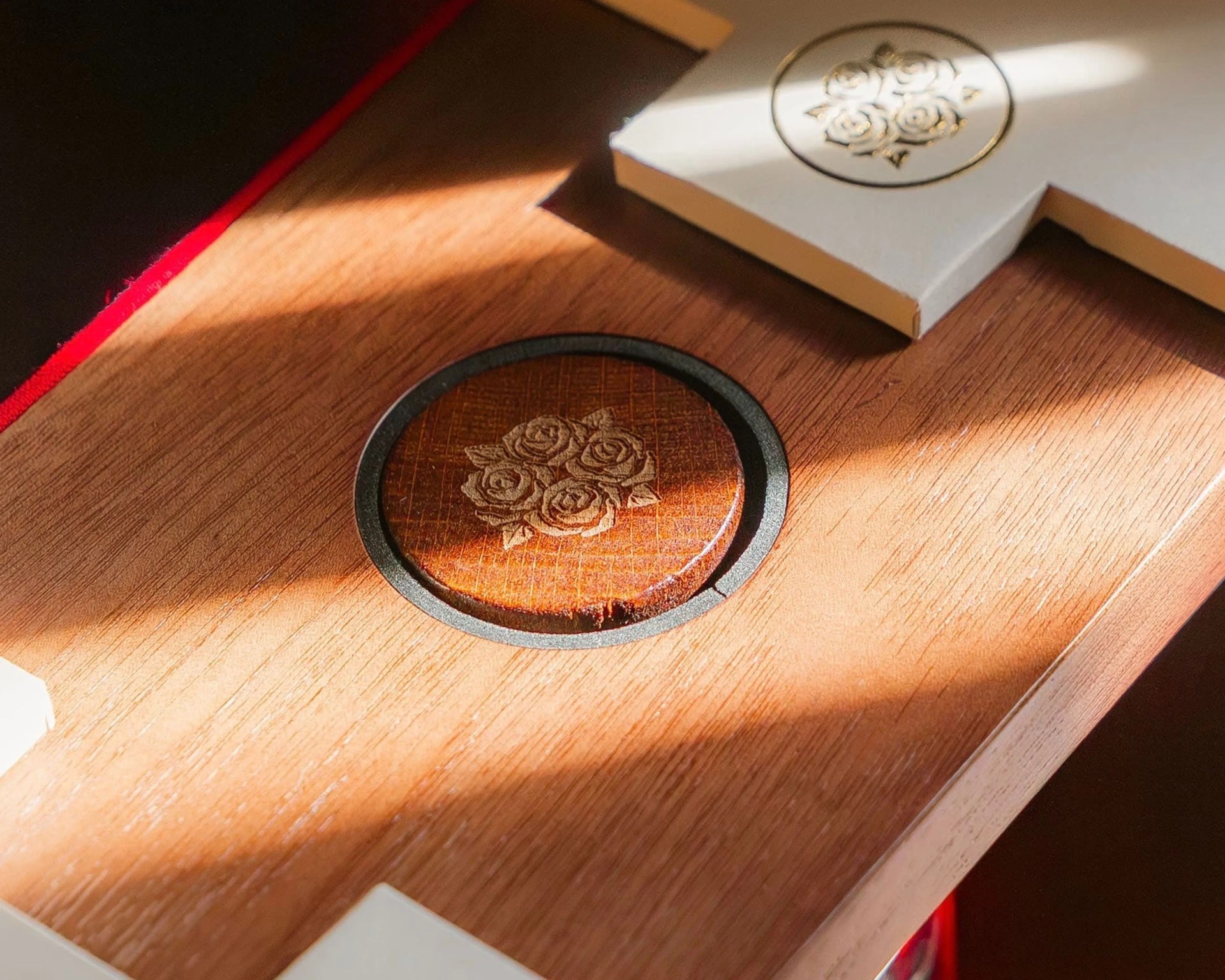 Wooden surface with a round wooden coaster featuring an engraved rose design and a white cross-shaped object with a similar rose engraving.