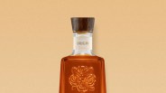 Amber glass bottle with embossed roses and a wooden cap labeled "Origin" on a beige background.