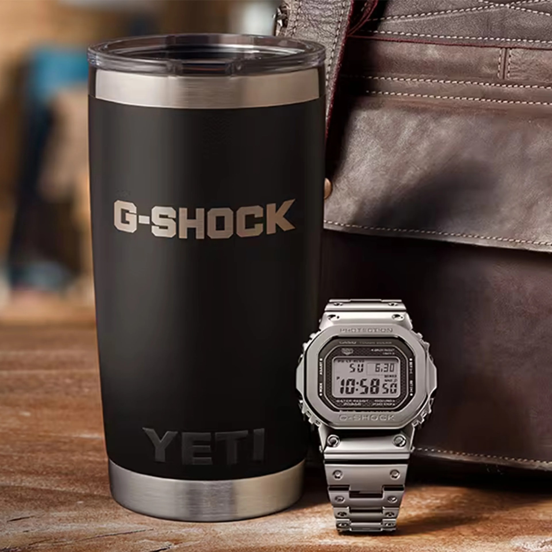 Stainless steel G-Shock digital watch next to a black Yeti tumbler with silver accents on a wooden surface.