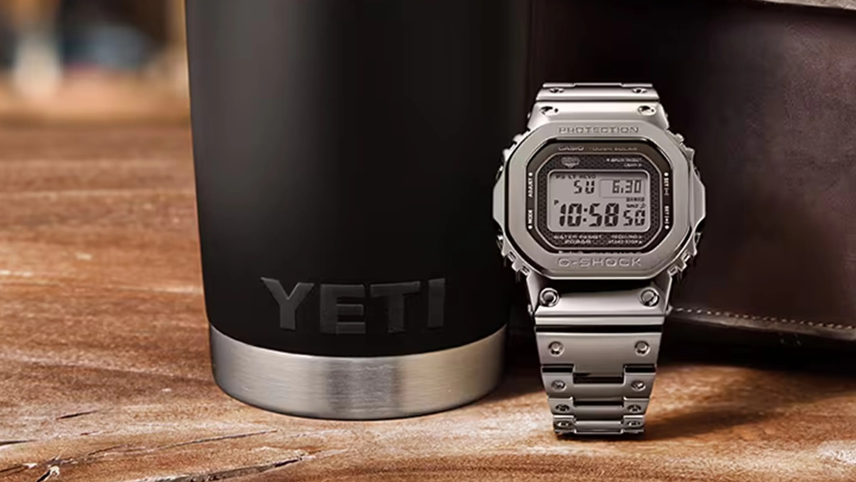 Stainless steel G-Shock digital watch next to a black YETI tumbler on a wooden surface.