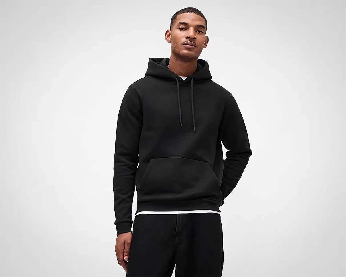 Man wearing a plain black hoodie with a front pocket and drawstrings over a white shirt.