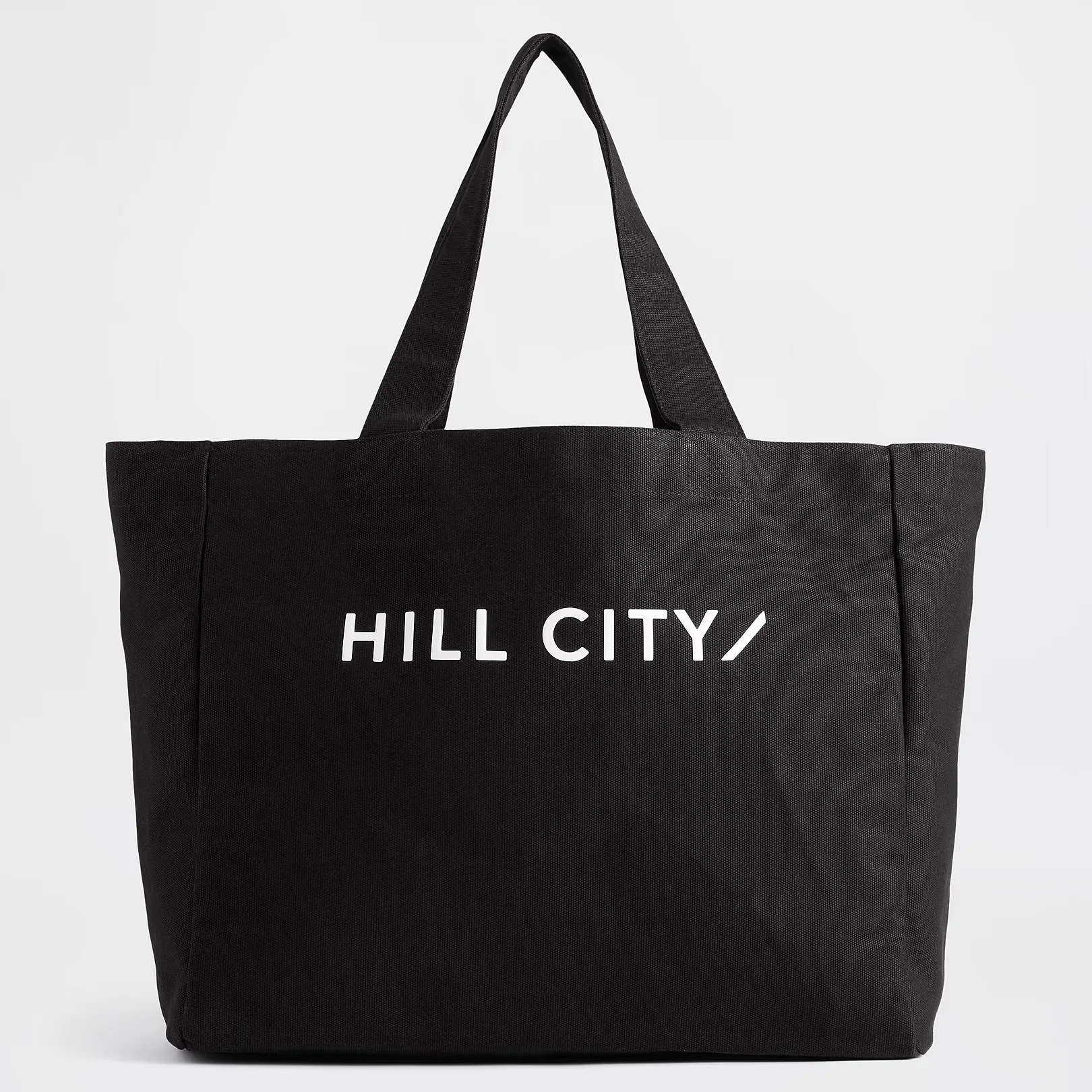 Black canvas tote bag with wide handles and white "HILL CITY" text on front.