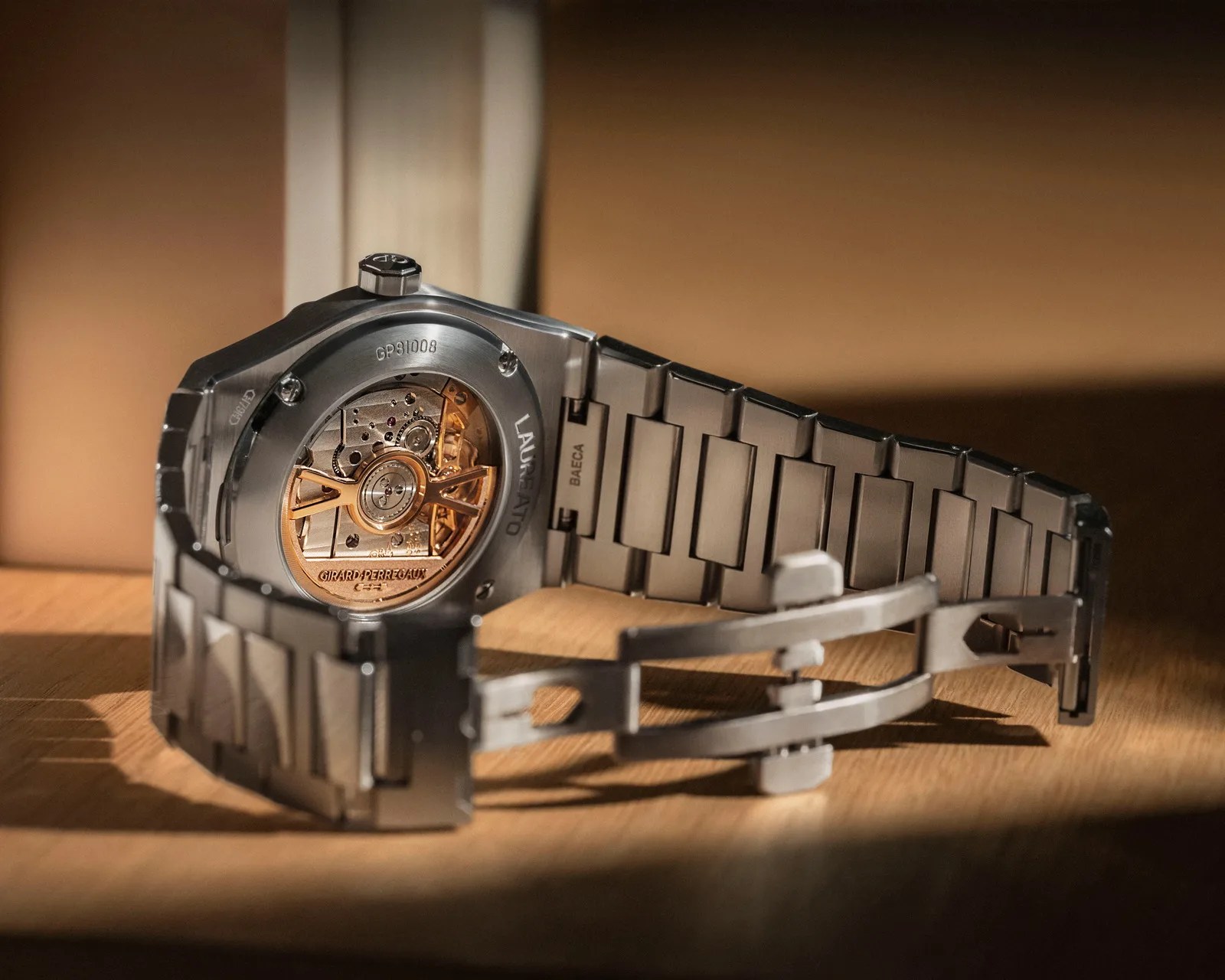 Stainless steel wristwatch with visible gold-toned mechanical movement and metal bracelet on a wooden surface.