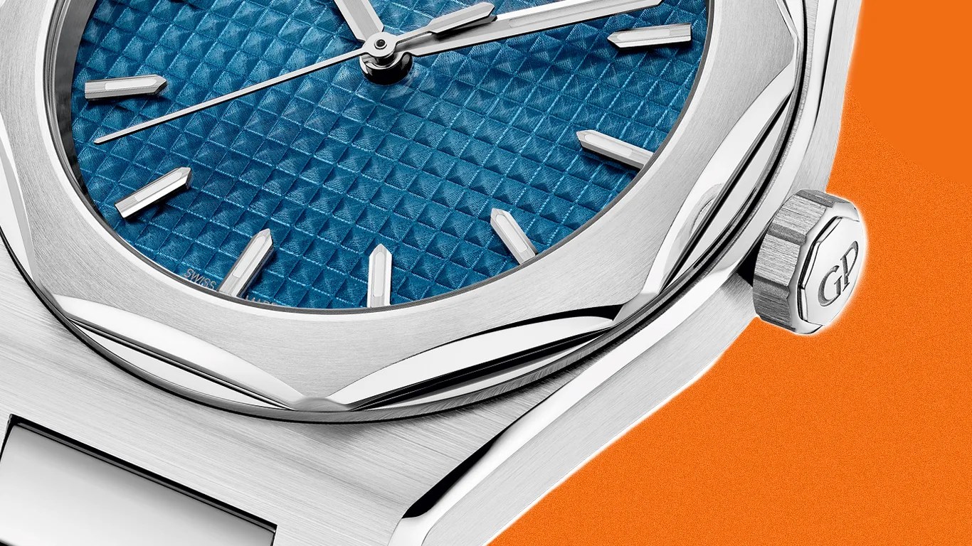 Close-up of a silver watch with a textured blue dial and silver hour markers on an orange background.