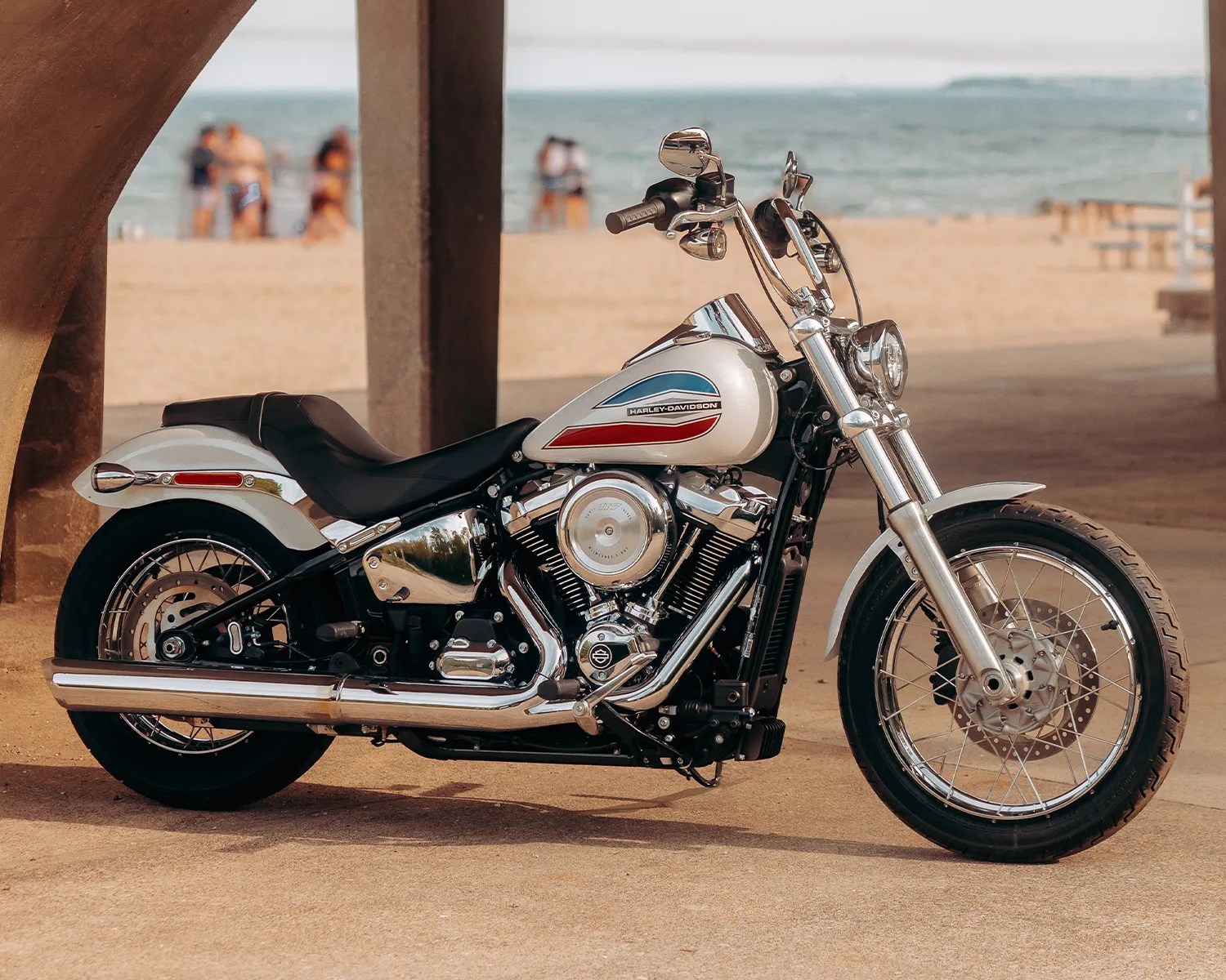 White and chrome Harley-Davidson motorcycle parked on a concrete surface near a beach.