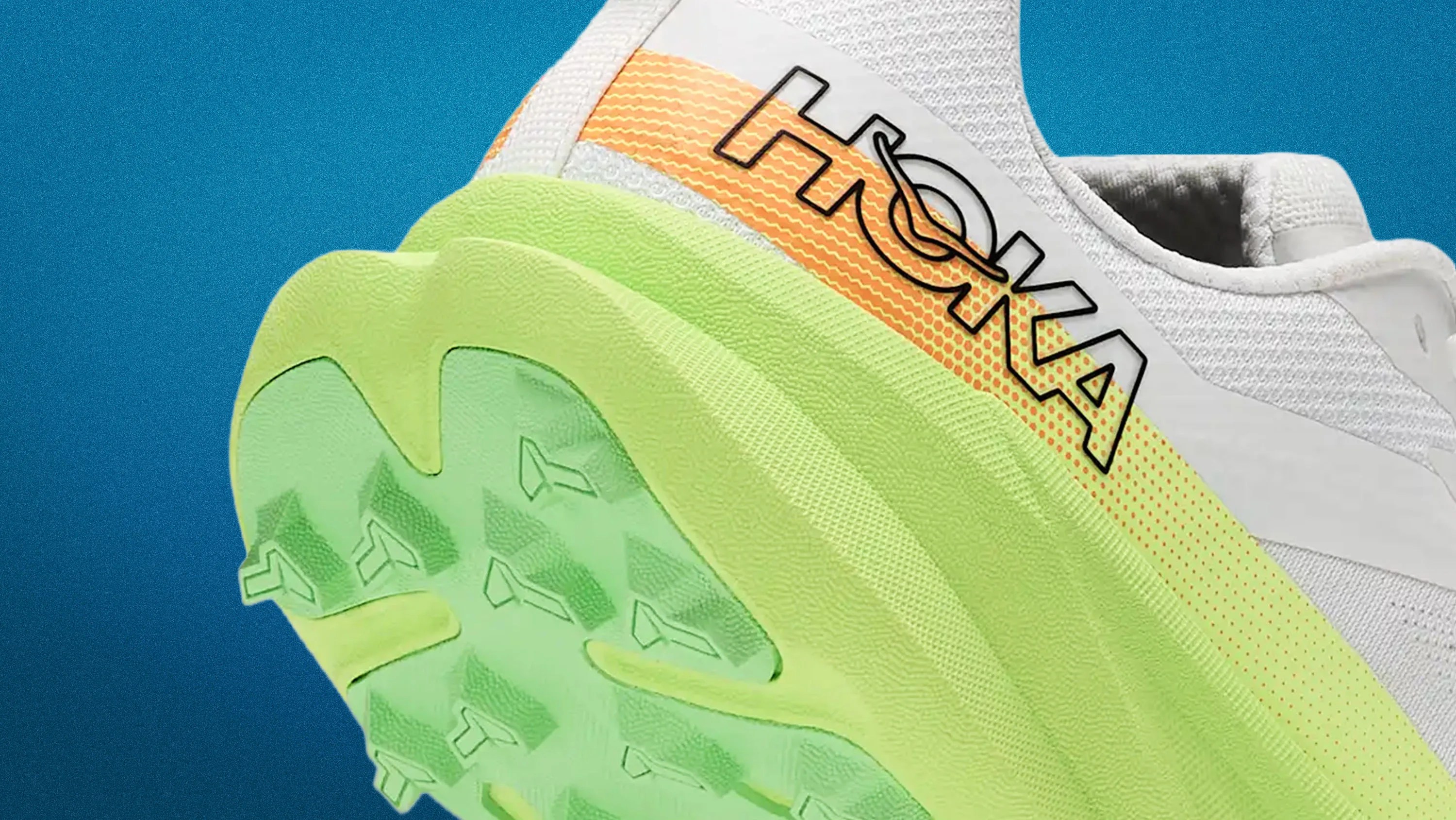 Close-up of a white HOKA sneaker with a green sole and orange-yellow gradient detail on the side.