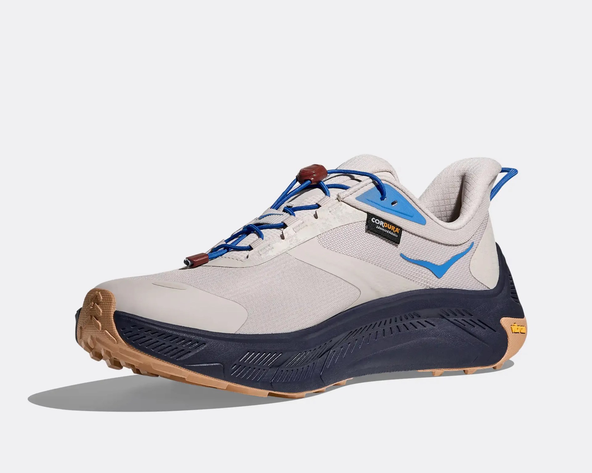 Light beige and blue athletic shoe with Cordura fabric tag, blue laces, and gum-colored sole with black midsole.