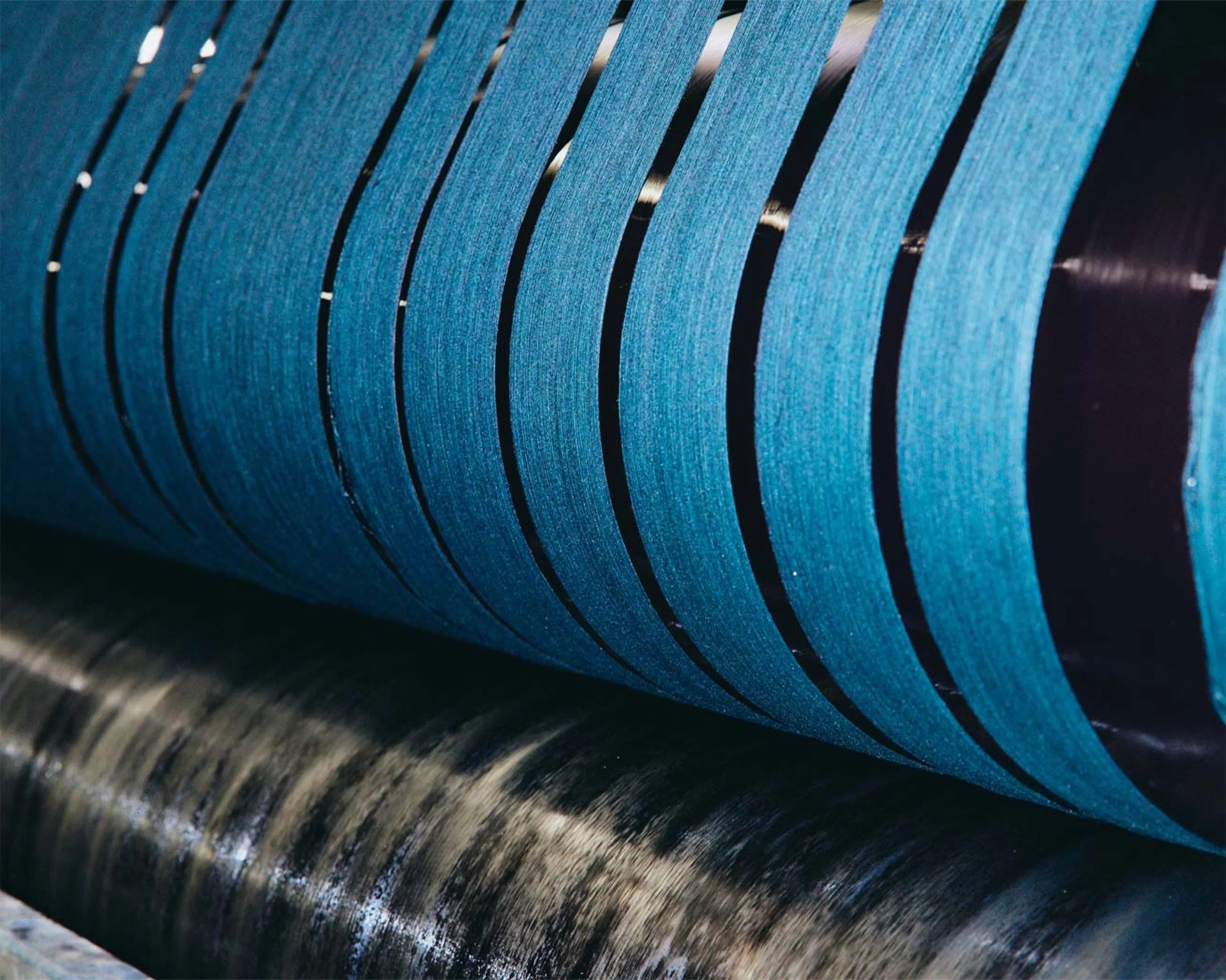 Close-up of blue abrasive sanding belts wrapped around a rotating drum.