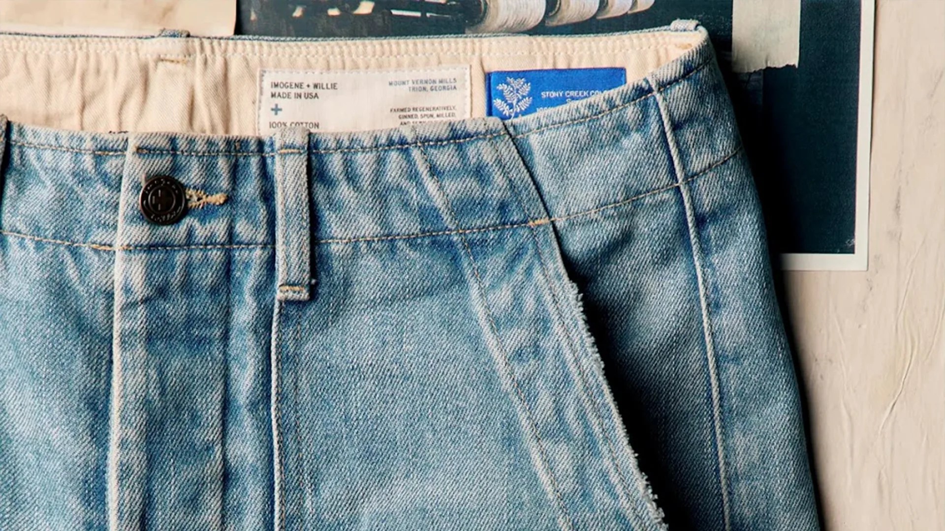 Light blue denim jeans with a black button and visible white fabric labels inside the waistband.