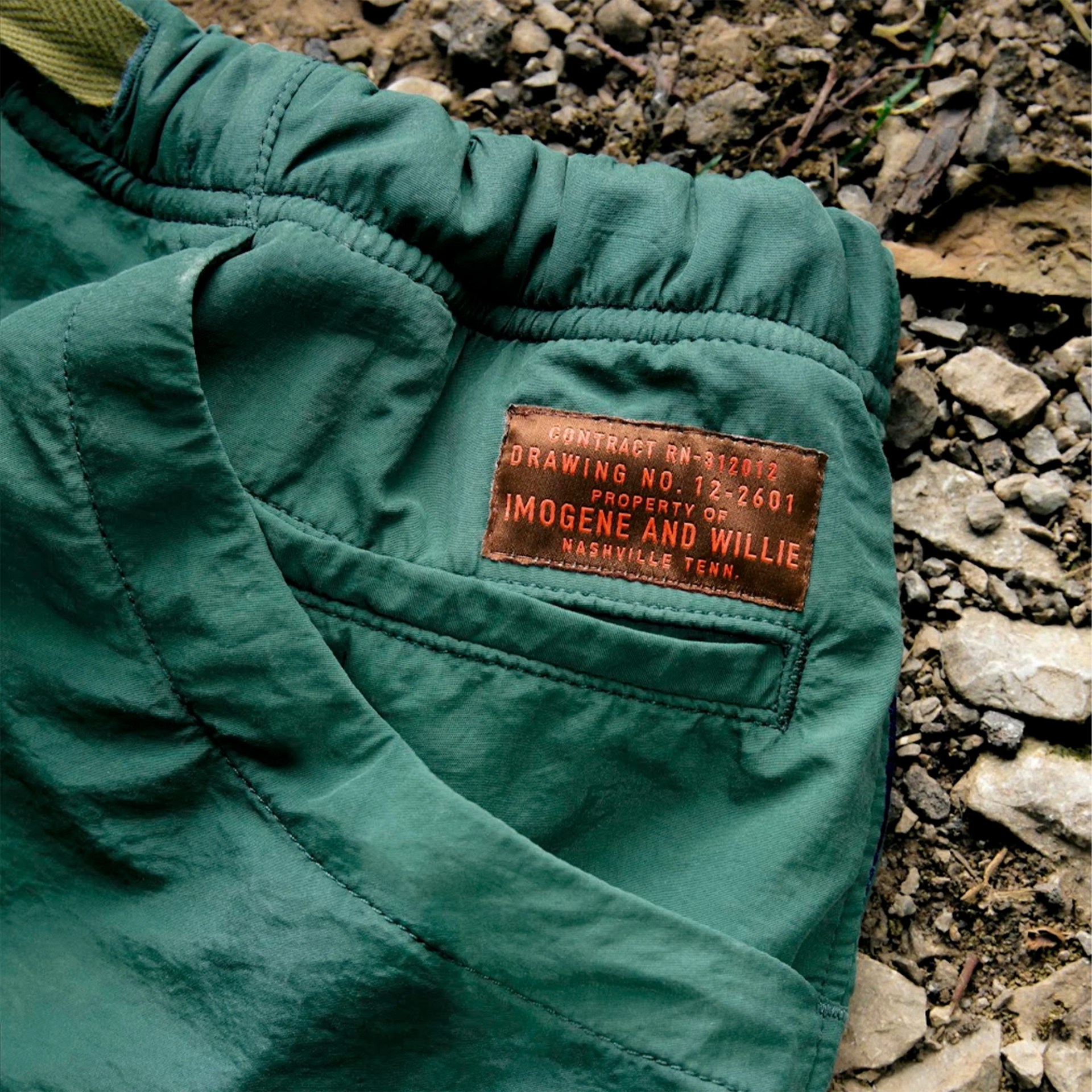 Green fabric with a brown leather patch label stitched on, lying on rocky ground.