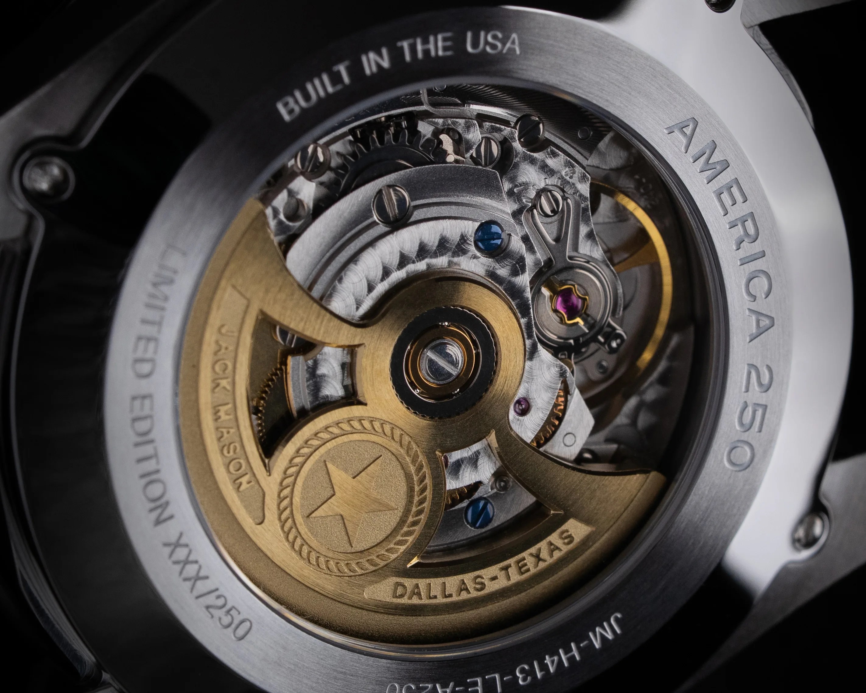 Close-up of a watch's mechanical movement with gold and silver components, engraved with "DALLAS-TEXAS" and "BUILT IN THE USA.