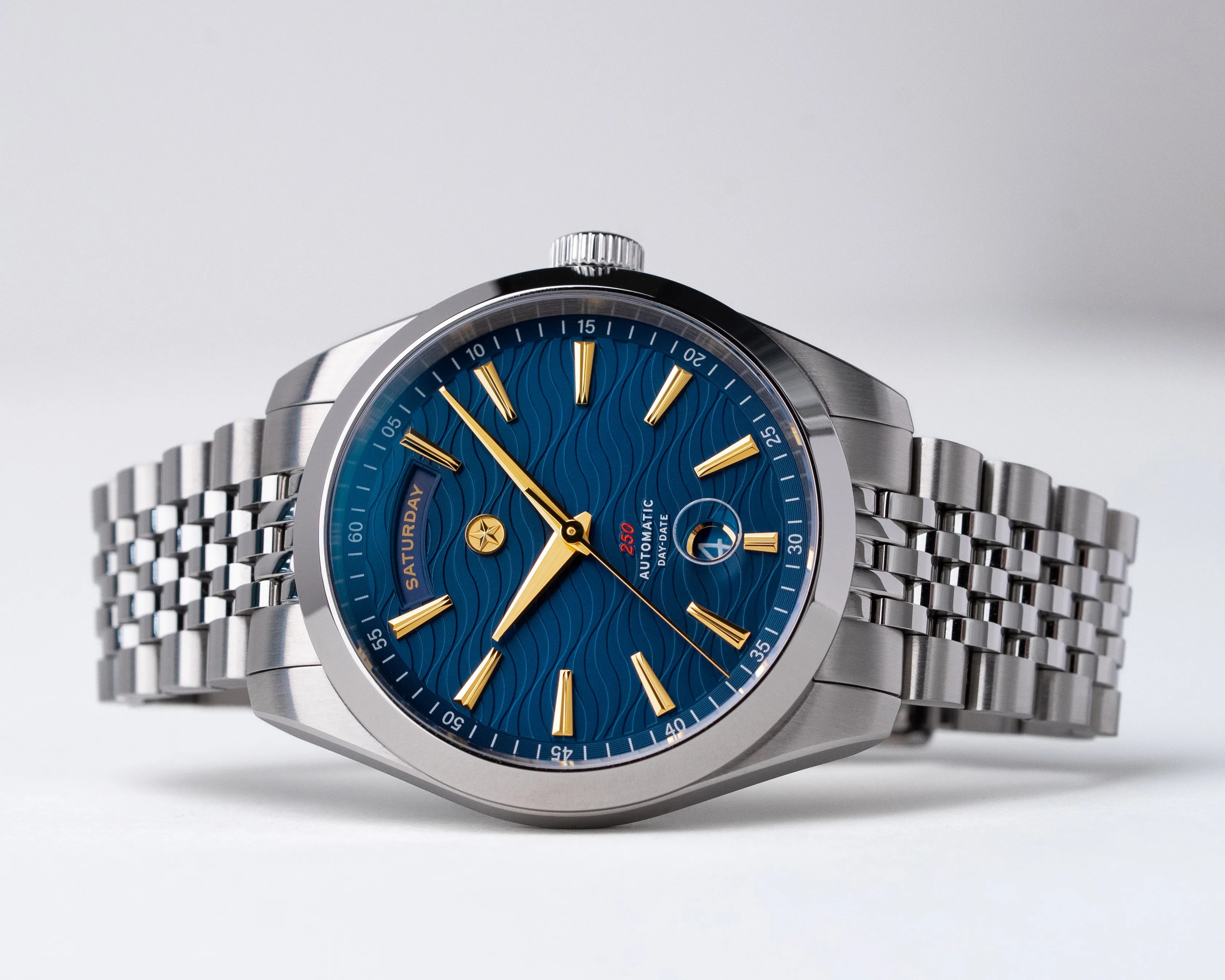 Silver metal wristwatch with a blue textured dial, gold hour markers and hands, and a day-date display.