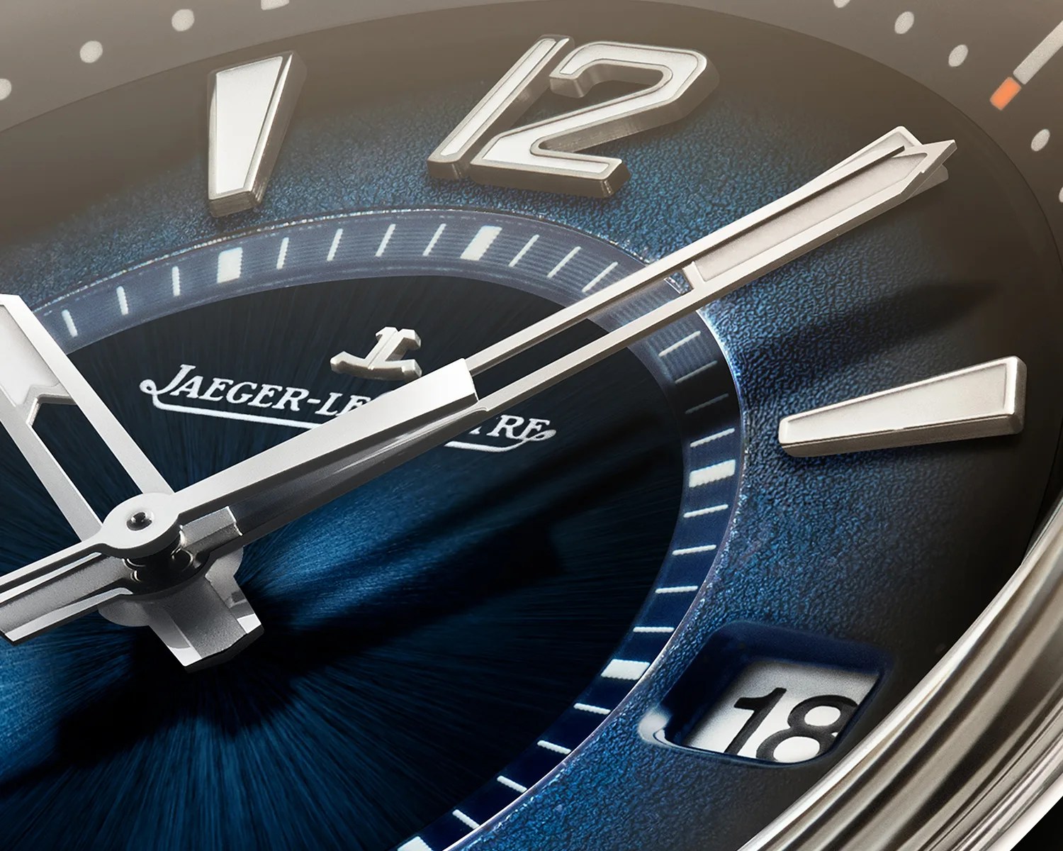 Close-up of a Jaeger-LeCoultre watch face with silver hands, blue textured dial, and date window showing 18.