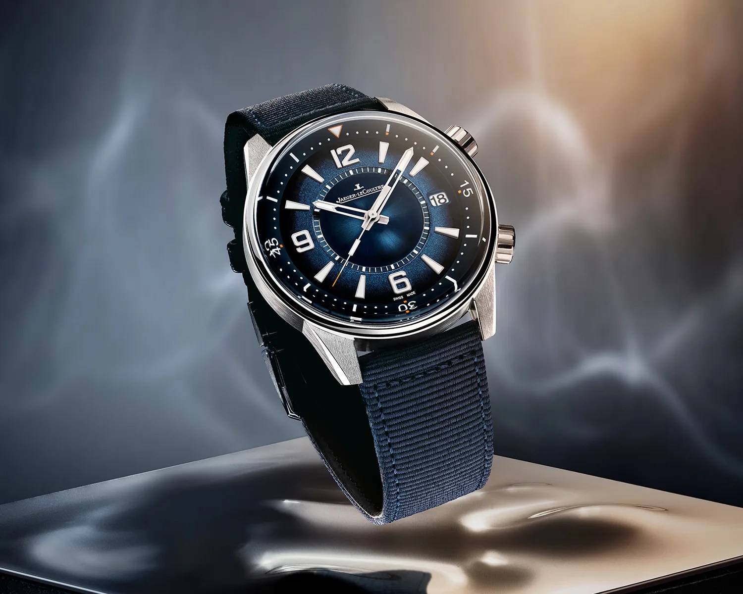 Silver Jaeger-LeCoultre watch with blue dial and fabric strap on reflective surface.