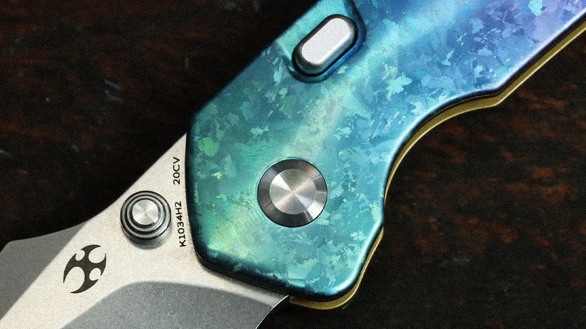 Close-up of a folding knife with a blue-green textured handle and a silver blade marked "K1034H2 20CV.