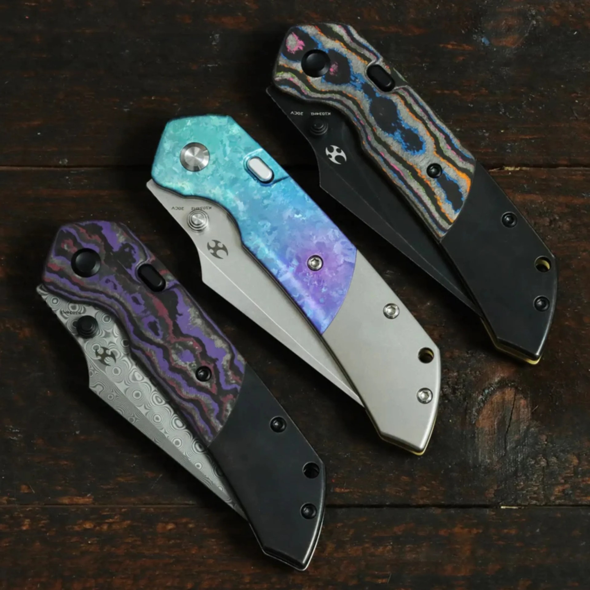 Four folding knives with colorful patterned handles in purple, blue, and multicolor on a dark wooden surface.
