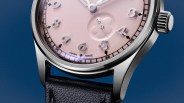Close-up of a wristwatch with a pink dial, silver numerals, stainless steel case, and black leather strap.