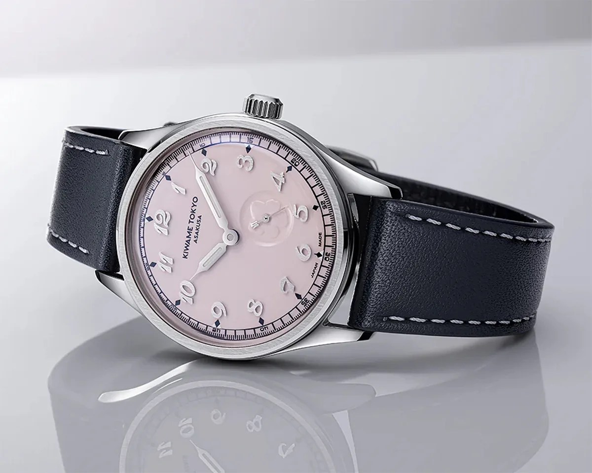 Silver wristwatch with a pale pink dial, white numerals, and black leather strap with white stitching.