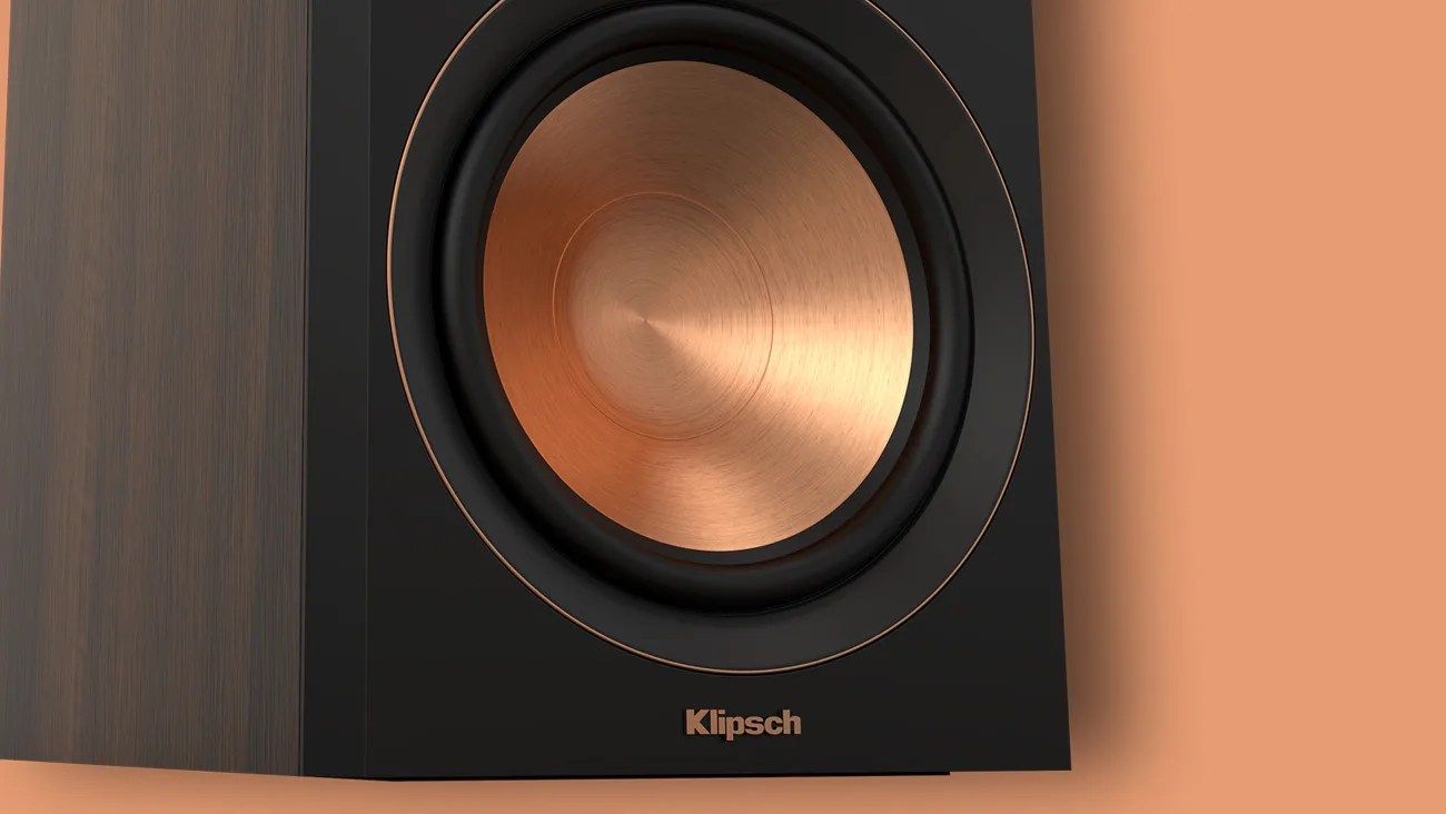 Close-up of a Klipsch speaker with a copper-colored cone and black frame on a wooden surface.