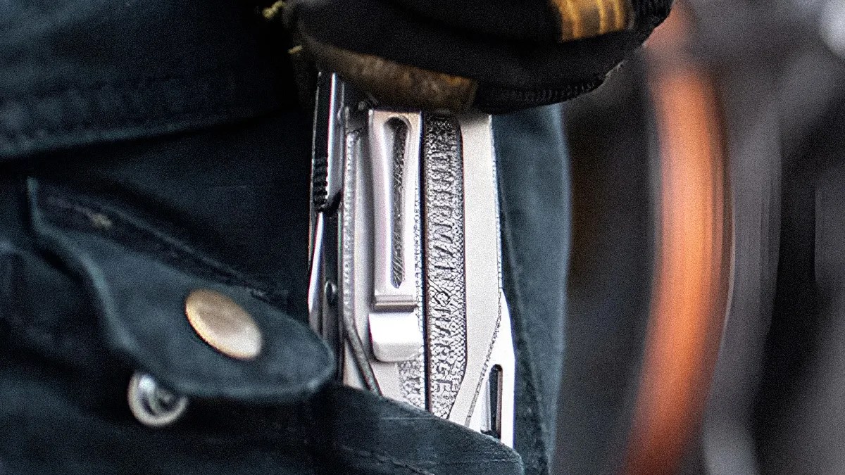 Close-up of a silver folding knife clipped inside a dark fabric pocket with a button.