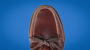 Brown leather moccasin shoe with visible stitching and tied laces on a blue background.