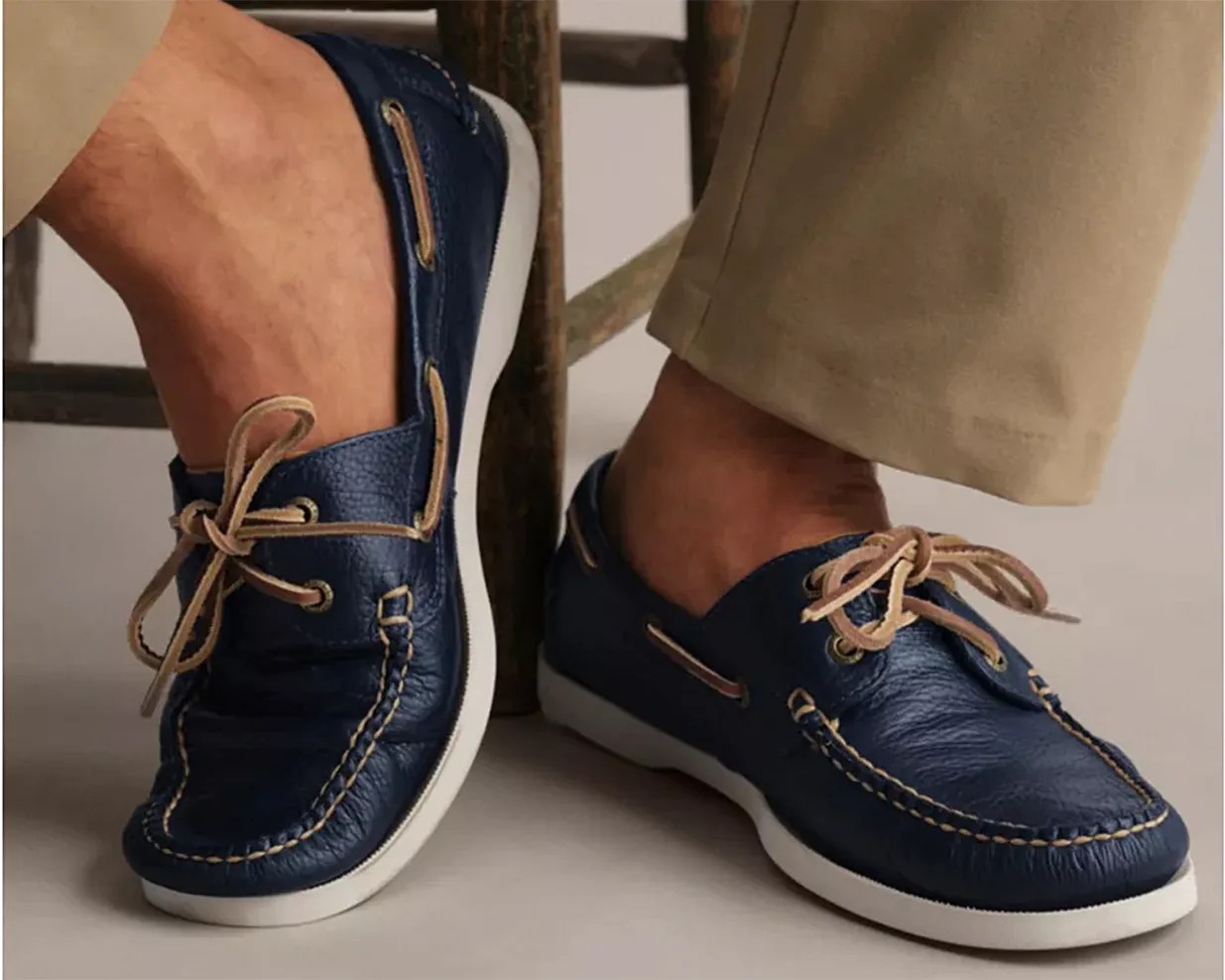 Navy blue leather boat shoes with tan laces and white soles worn with beige pants.