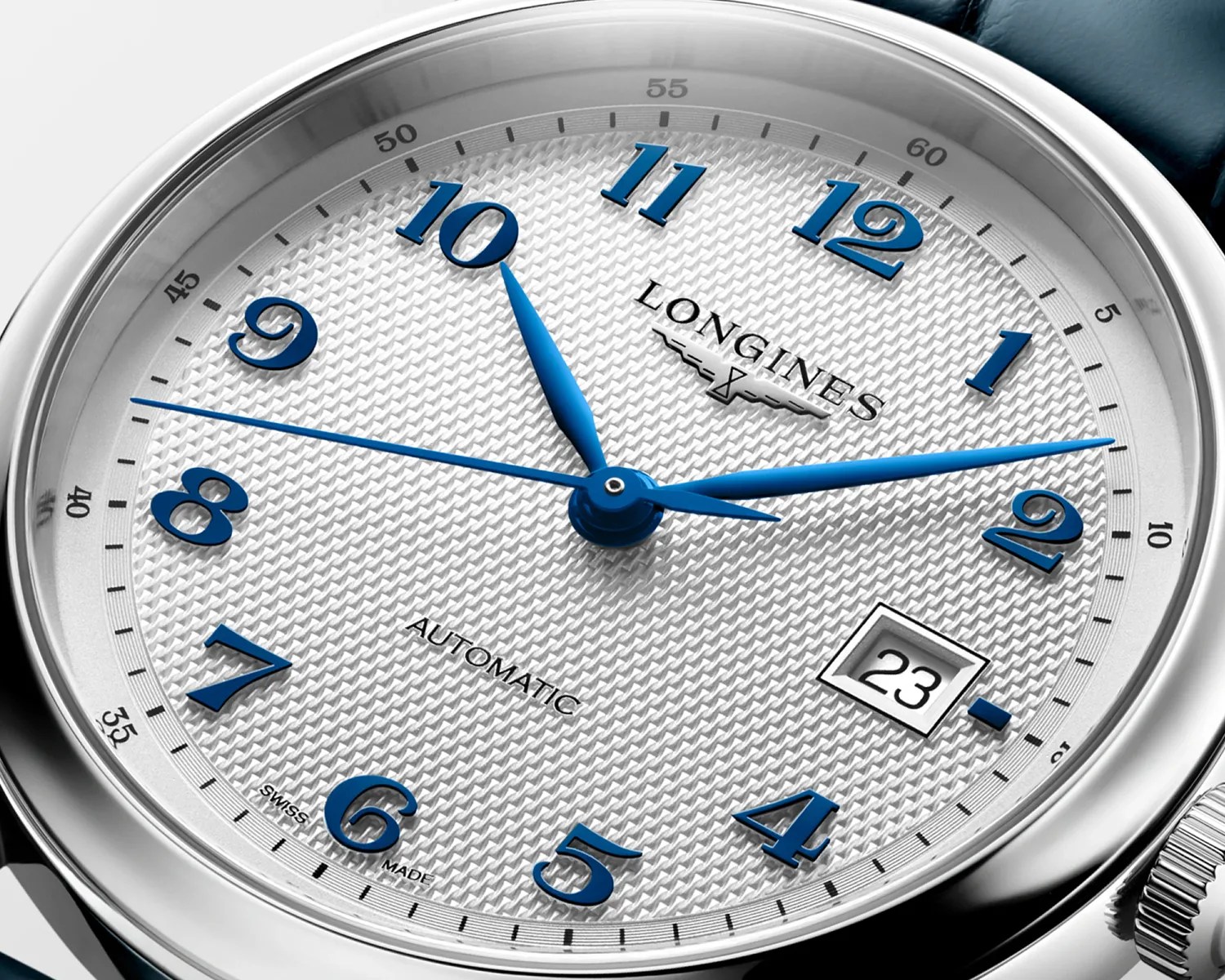 Close-up of a Longines watch face with blue numerals and hands, a textured white dial, and a date window showing 23.