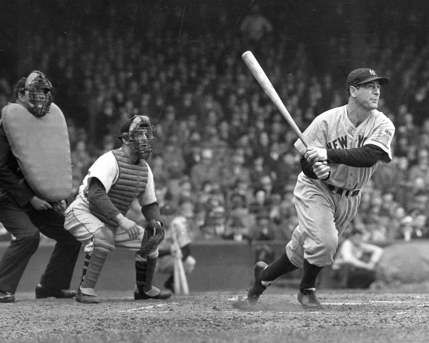 Black-and-white photo of a New York Yankees batter swinging a bat with a catcher and umpire behind home plate.