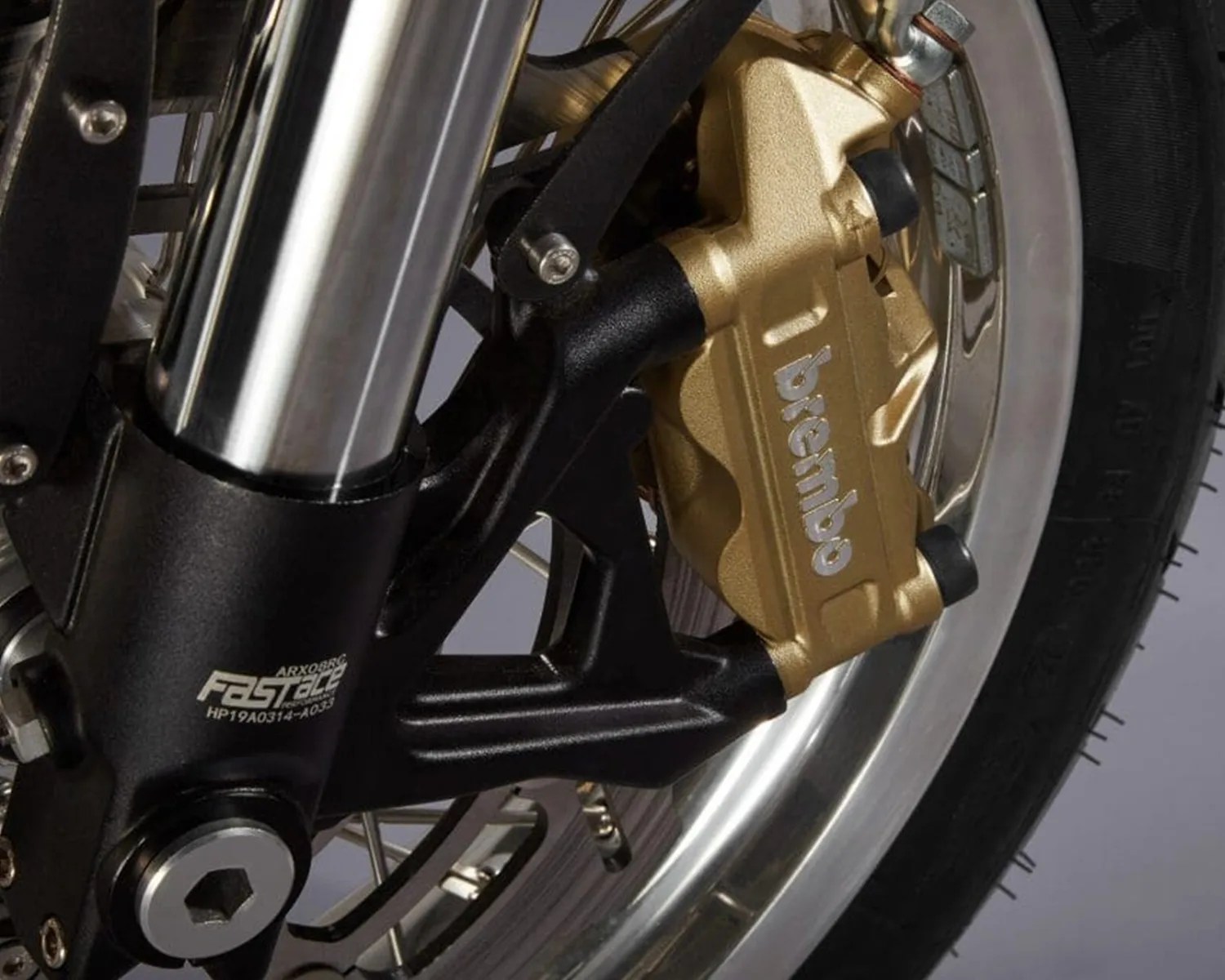 Close-up of a gold Brembo brake caliper mounted on a motorcycle wheel with a black suspension fork labeled "FAST ACE.