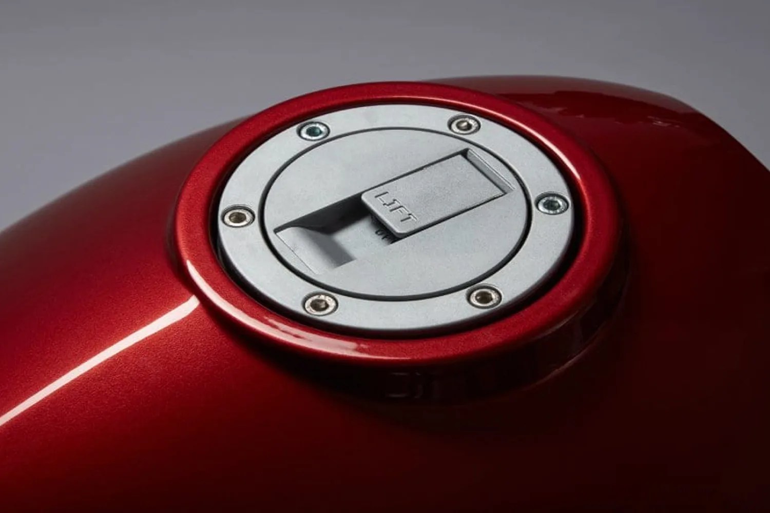 Silver circular fuel cap with "LIFT" text on a metallic red motorcycle fuel tank.