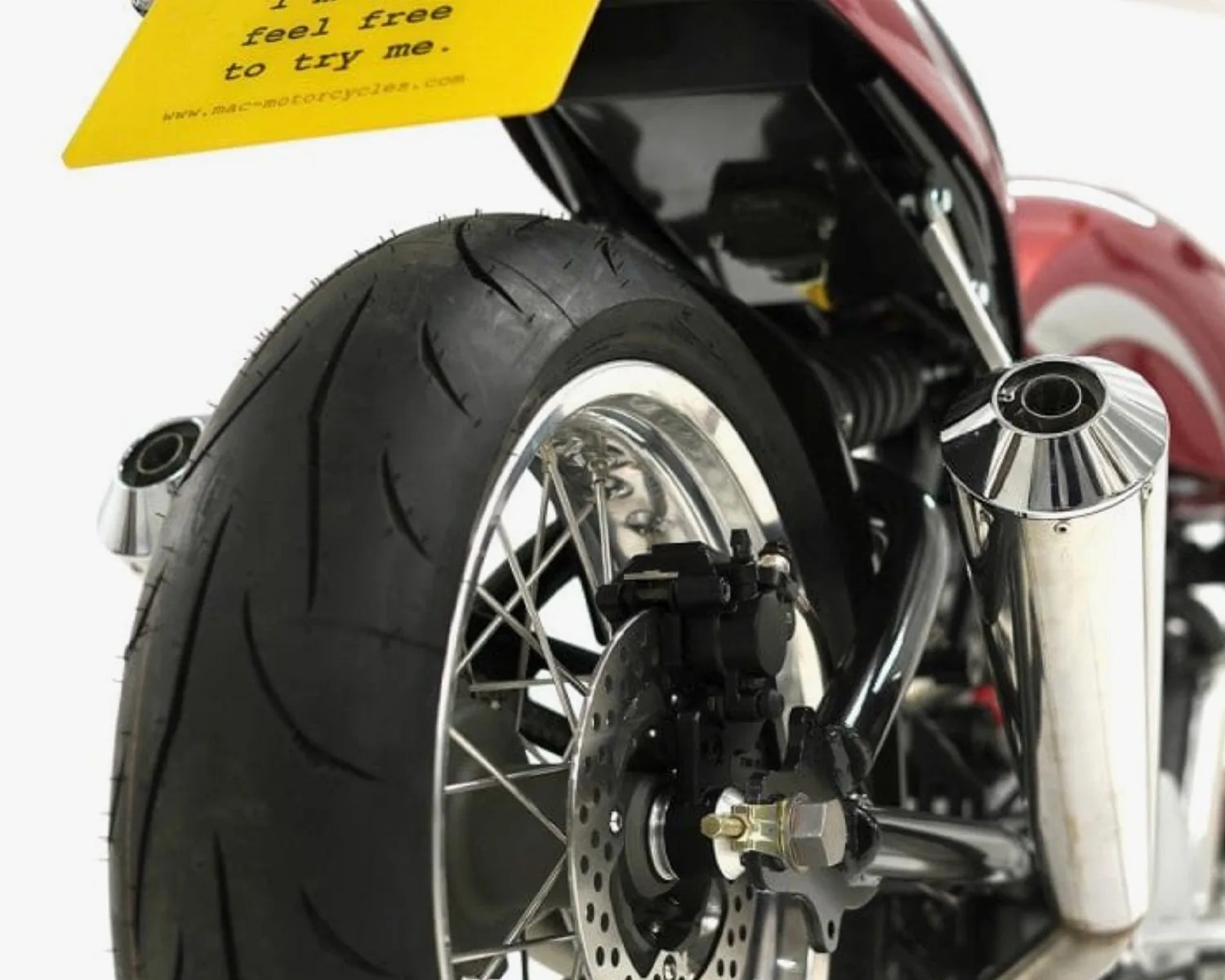 Close-up of a motorcycle's rear wheel with a black tire, silver spokes, disc brake, and chrome exhaust pipe.