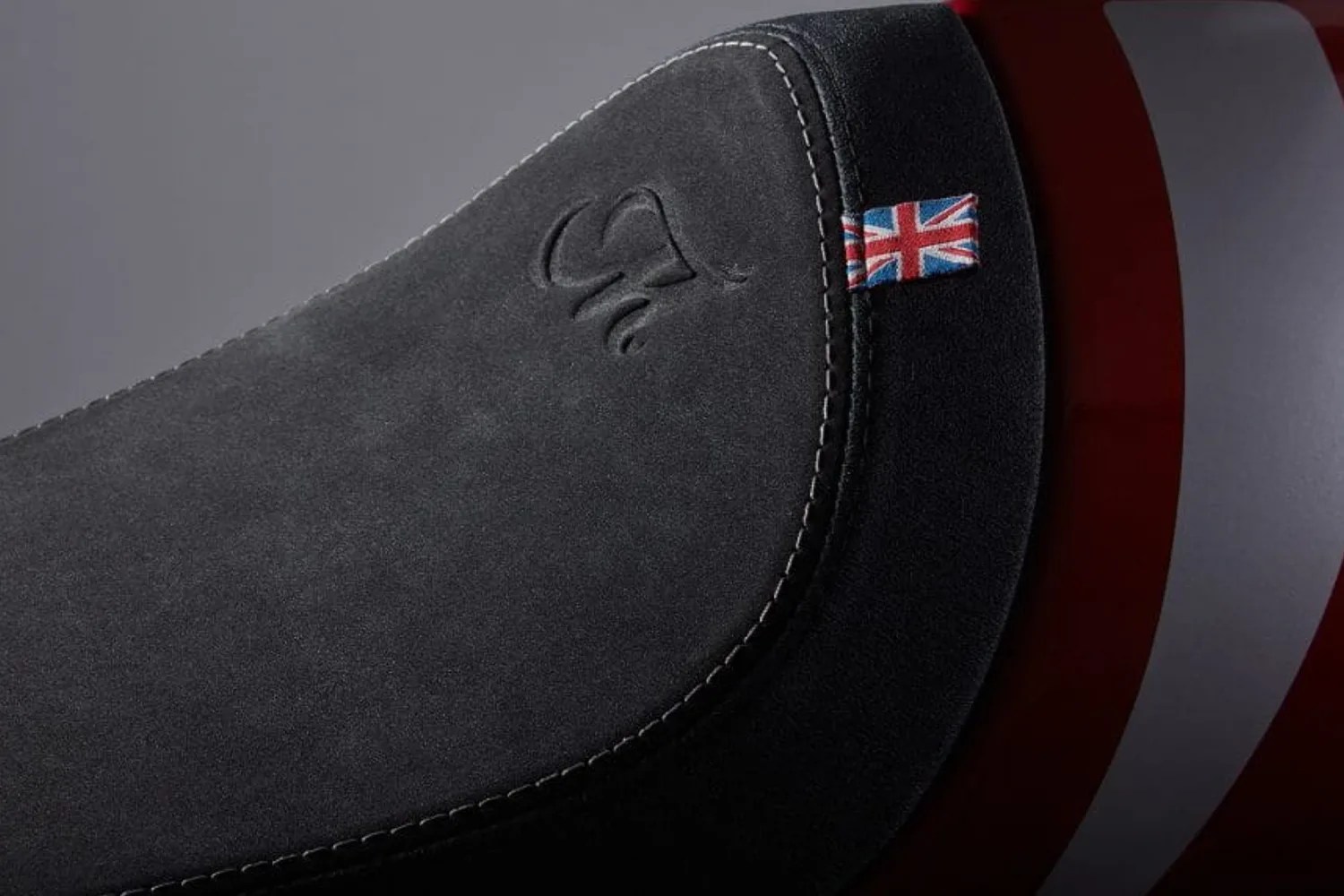 Close-up of a black suede motorcycle seat with white stitching and a small Union Jack flag tag.