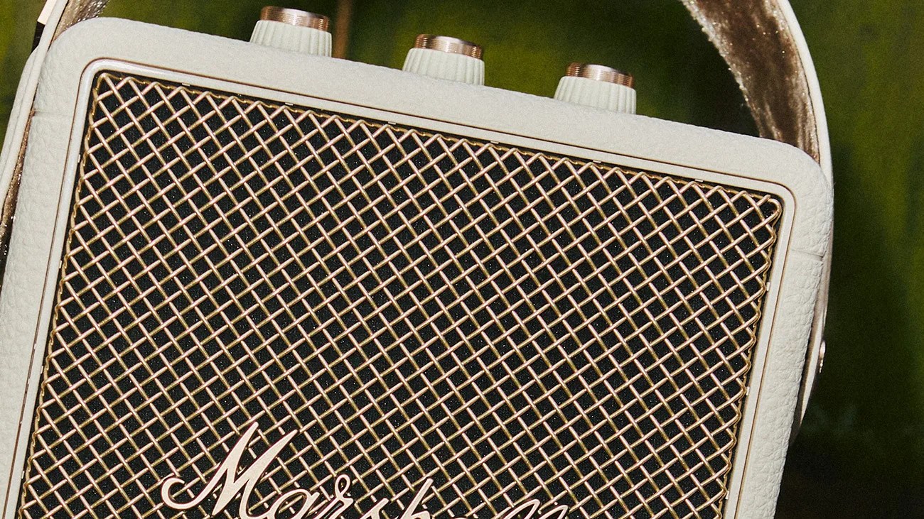Close-up of a white vintage-style portable speaker with a gold mesh grille and three white knobs on top.