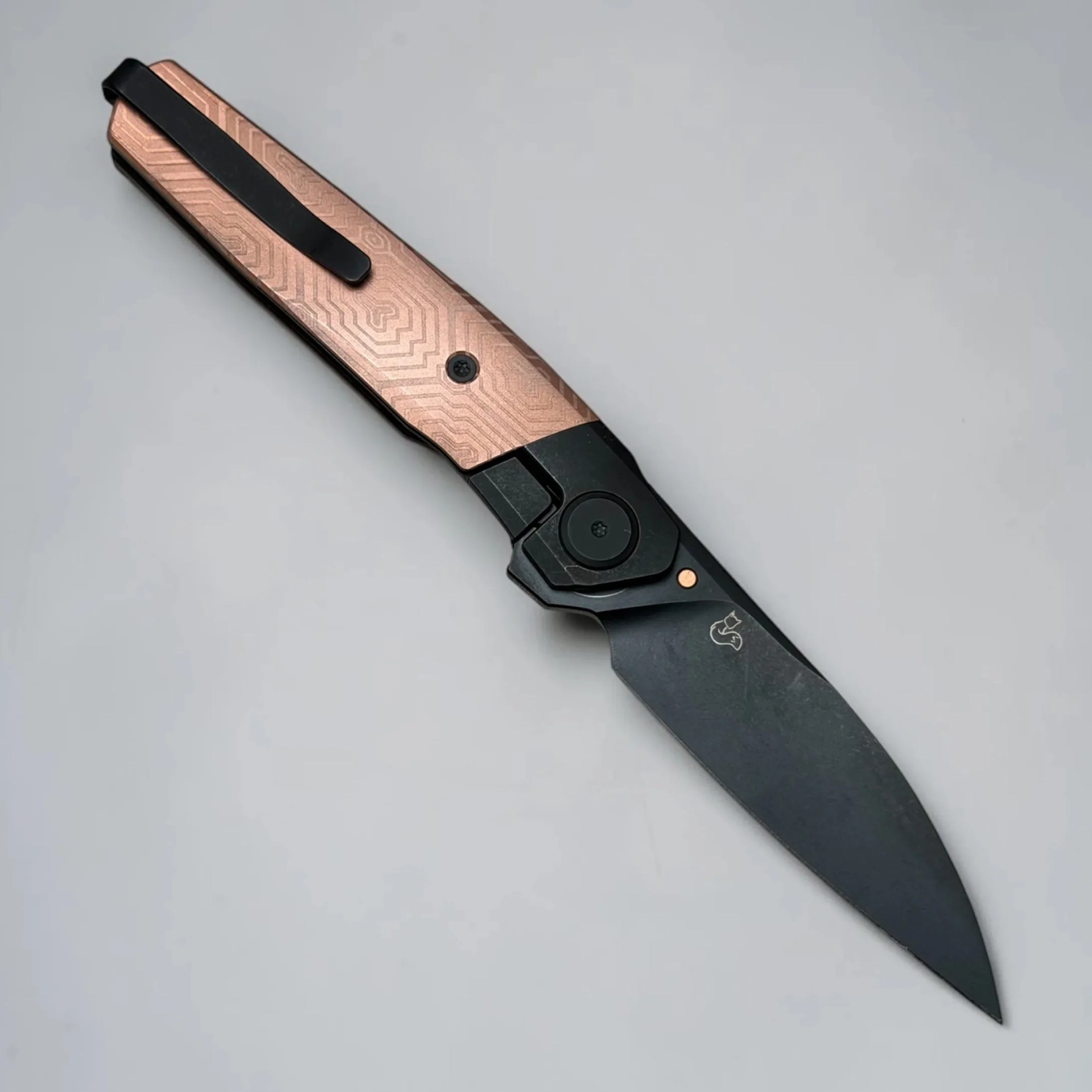 Black folding knife with a copper-toned handle featuring a geometric pattern and a black clip.
