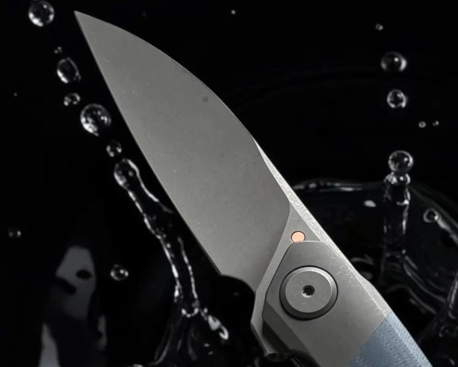 Close-up of a gray folding knife blade with a blue handle and water droplets in the background.