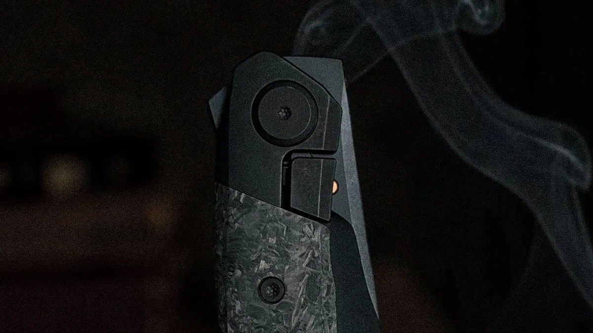 Close-up of a black and textured gray folding knife with smoke rising in the background.