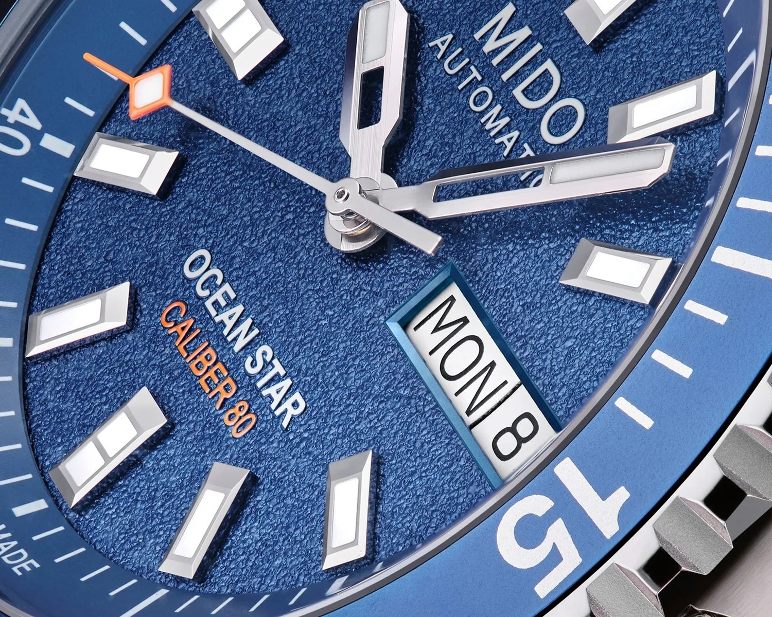 Close-up of a blue textured dial Mido Ocean Star Caliber 80 automatic watch with silver hands and markers, and a day-date window showing "MON 8".