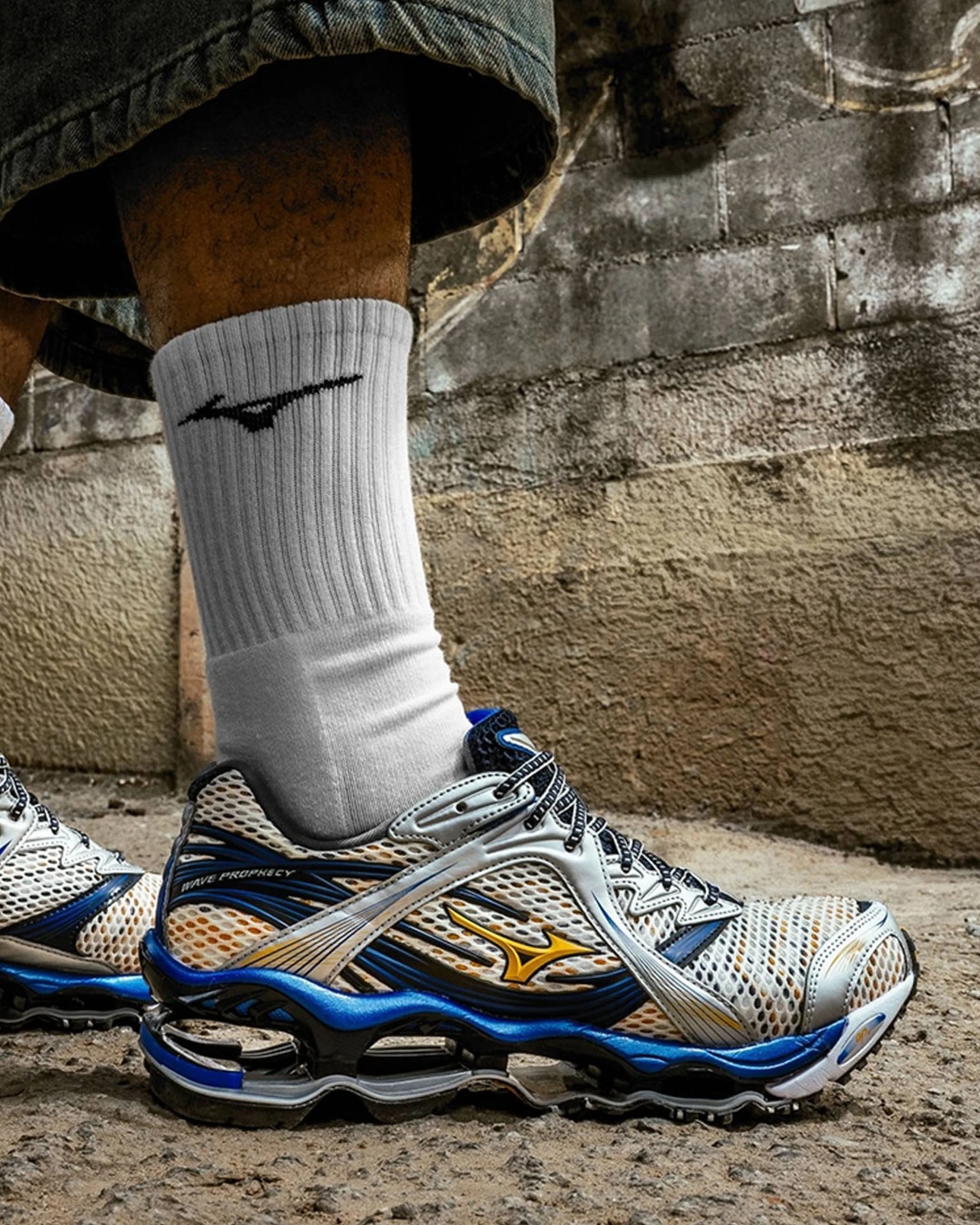 White and blue Mizuno Wave Prophecy running shoe with yellow logo worn with white socks.