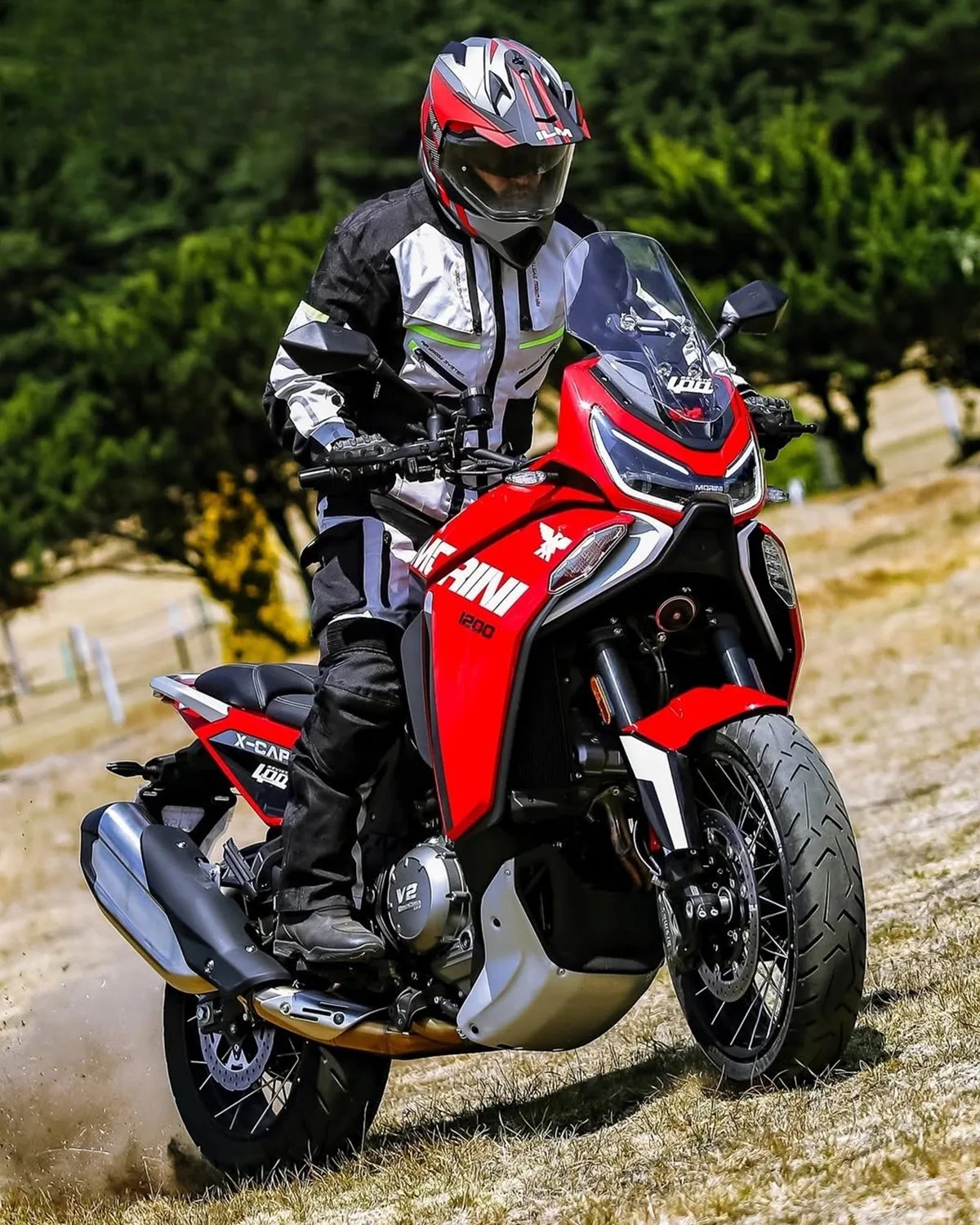 Rider in black and white gear on a red Macni 1200 V2 motorcycle on a grassy path.