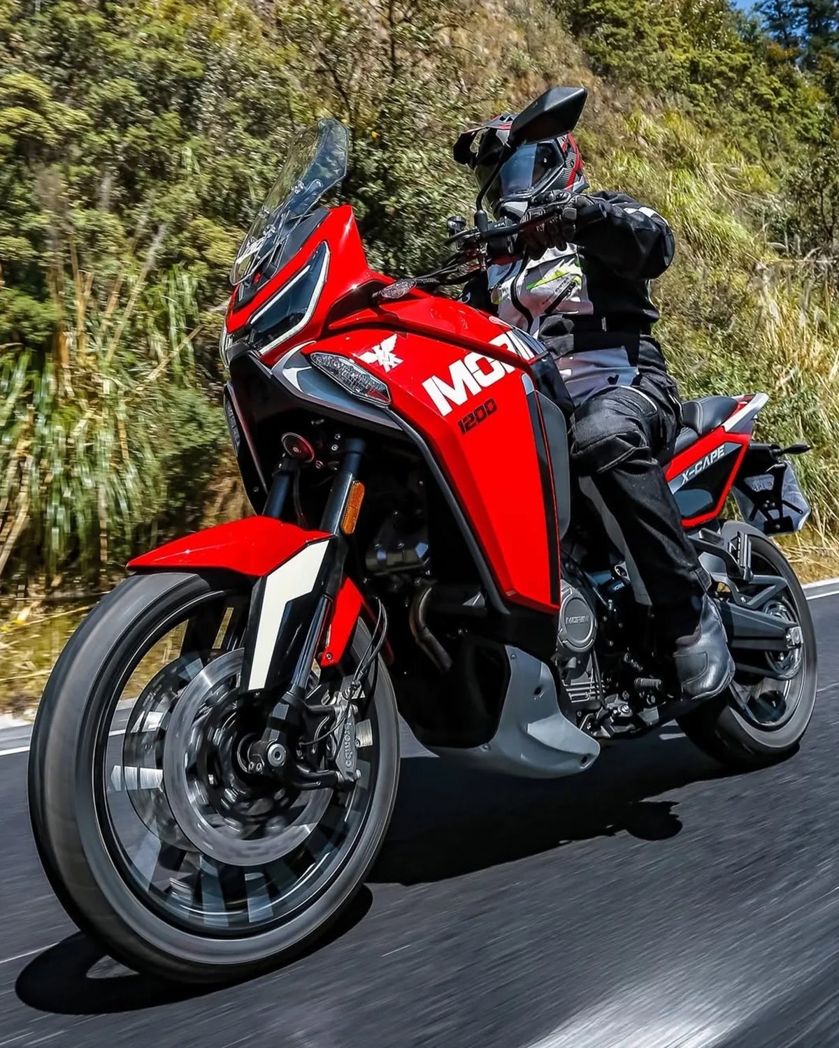 Red and black X-Cape 1200 motorcycle with rider wearing black and white gear on a road.